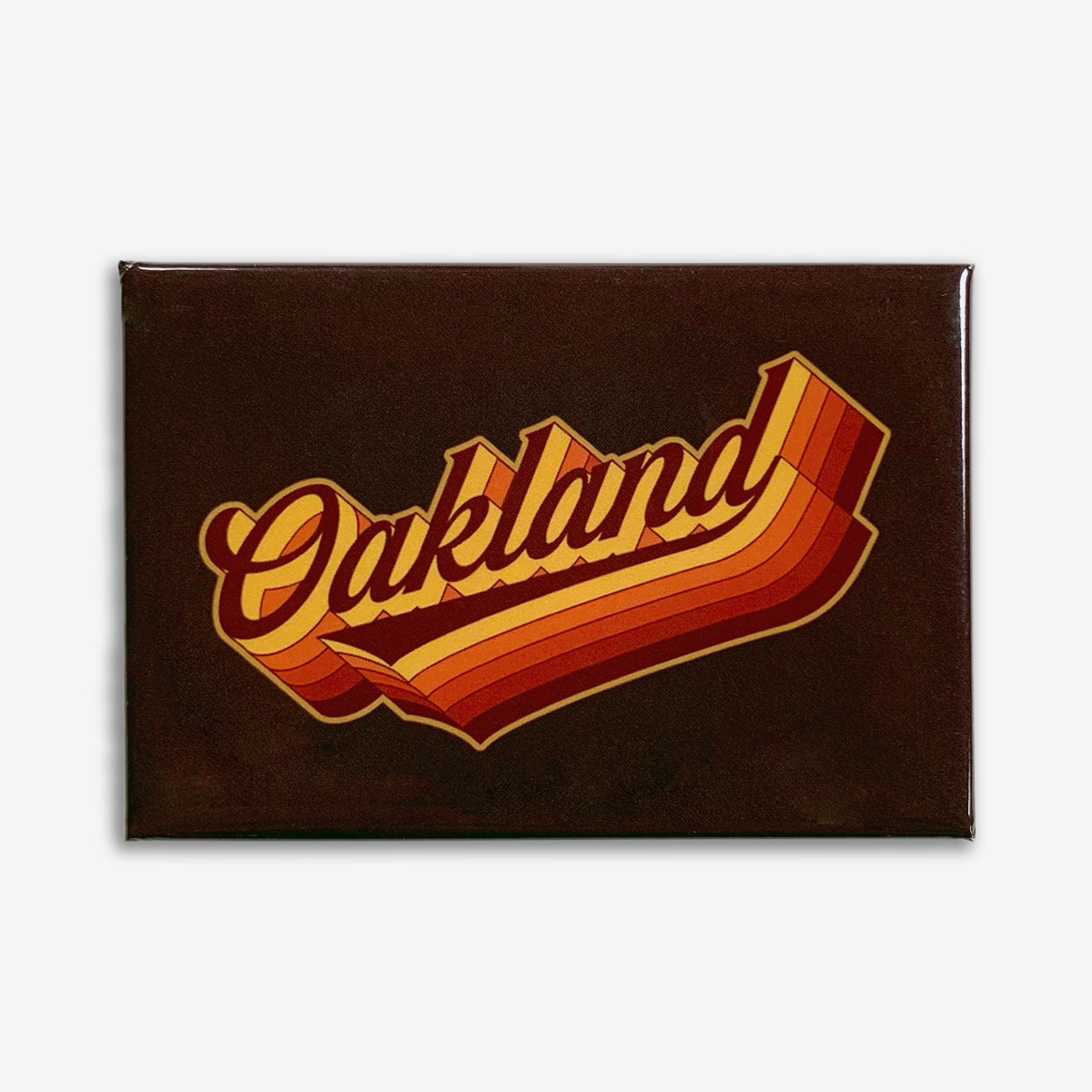 The Swash Magnet by Oaklandish is a rectangular, vintage-styled refrigerator magnet that features the word "Oakland" in a retro-style font. The text is designed with curved lines in shades of orange, yellow, and red, creating a warm gradient effect. The background is a solid dark brown or black, making the colorful text stand out prominently.