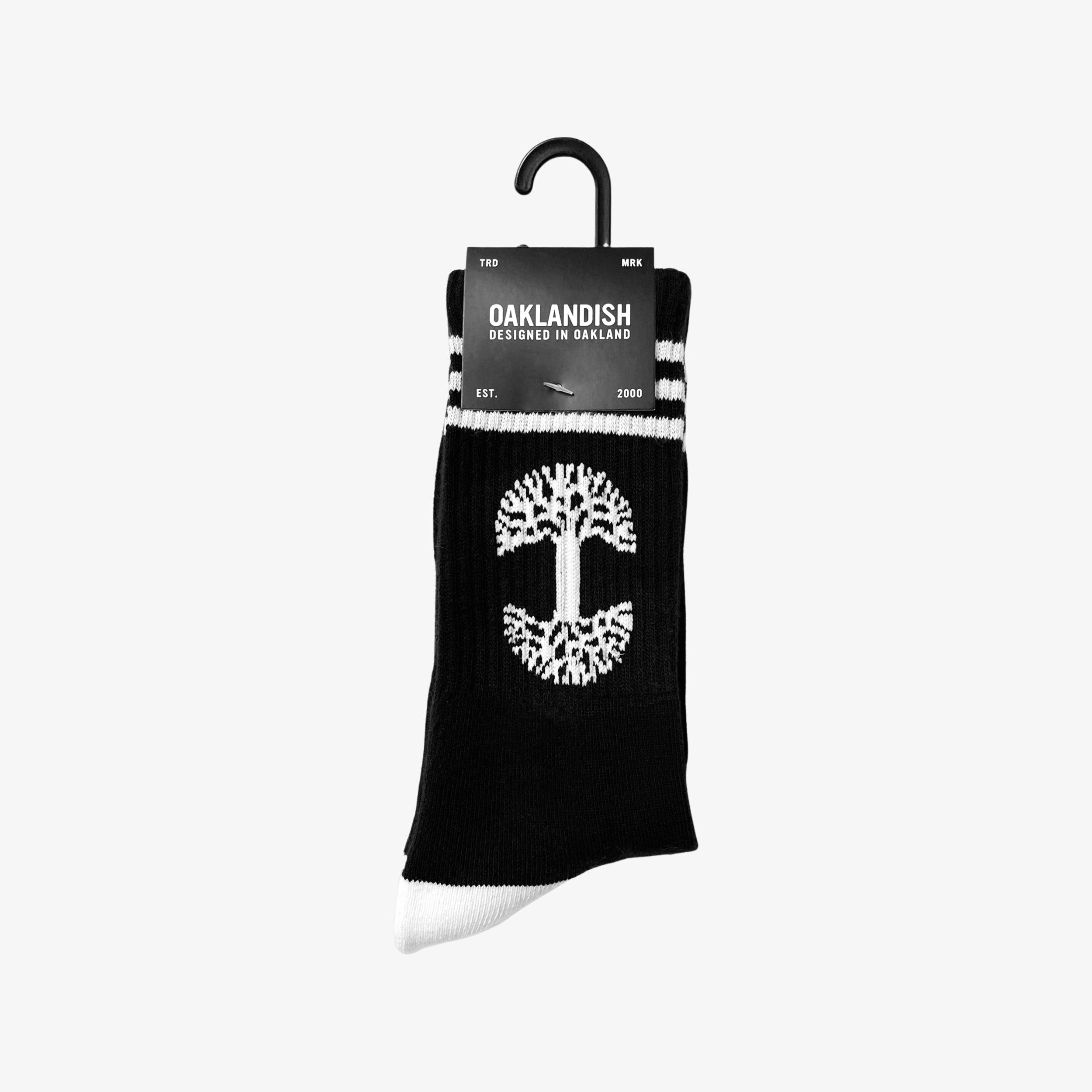 Black crew socks with a white Oaklandish tree logo and white ankle stripes in Oaklandish retail packaging.