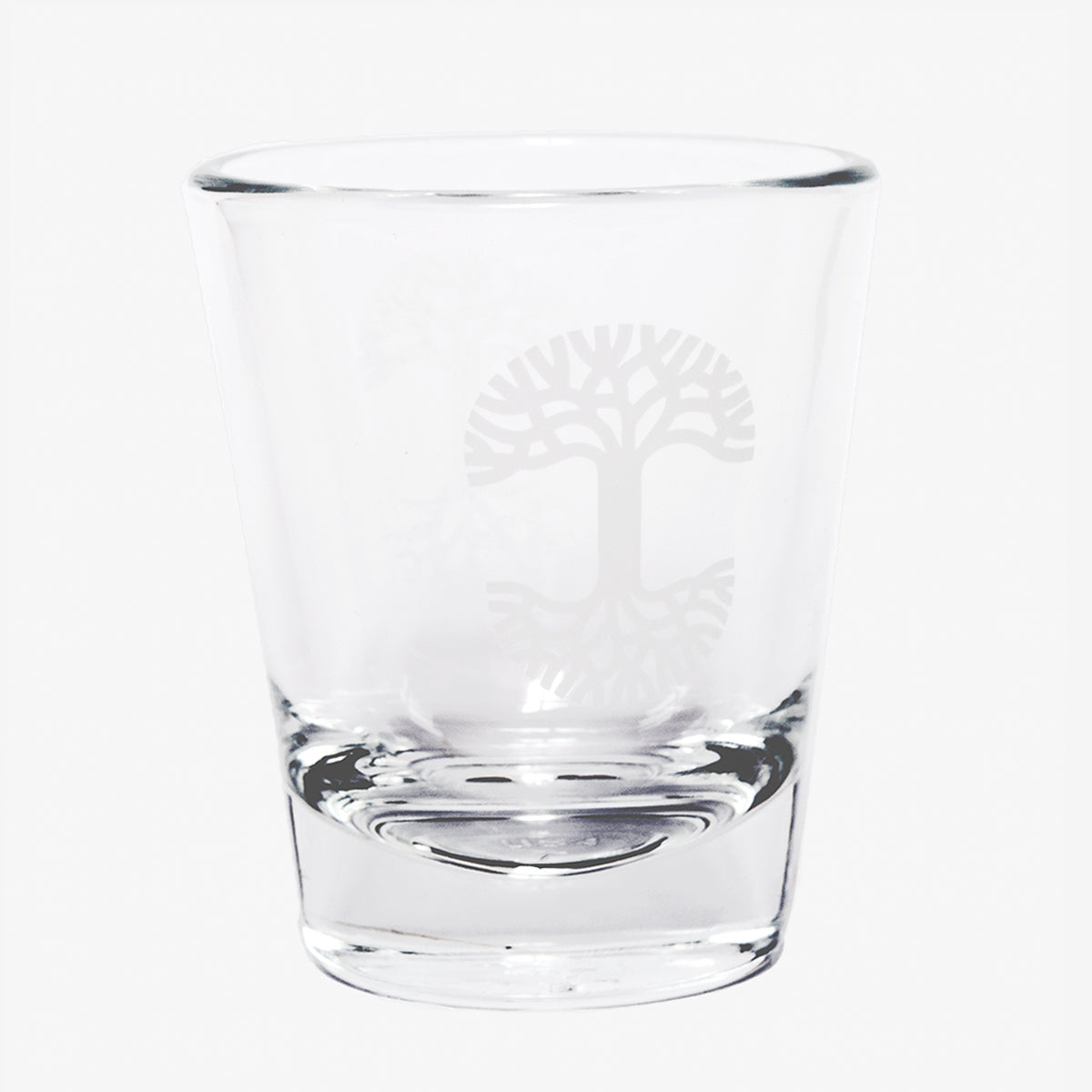 Clear glass liquor shot glass with translucent Oaklandish tree logo on the side.