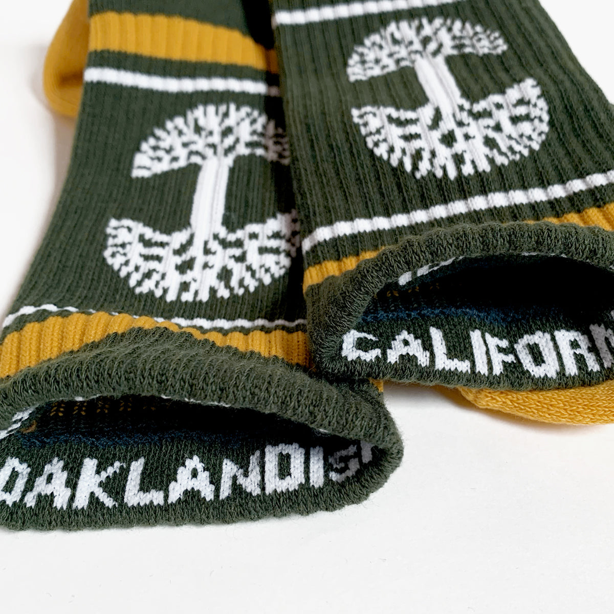 The top of green Oaklandish crew socks exposing OAKLAND and CALIFORNIA wordmarks on the inner cuffs.
