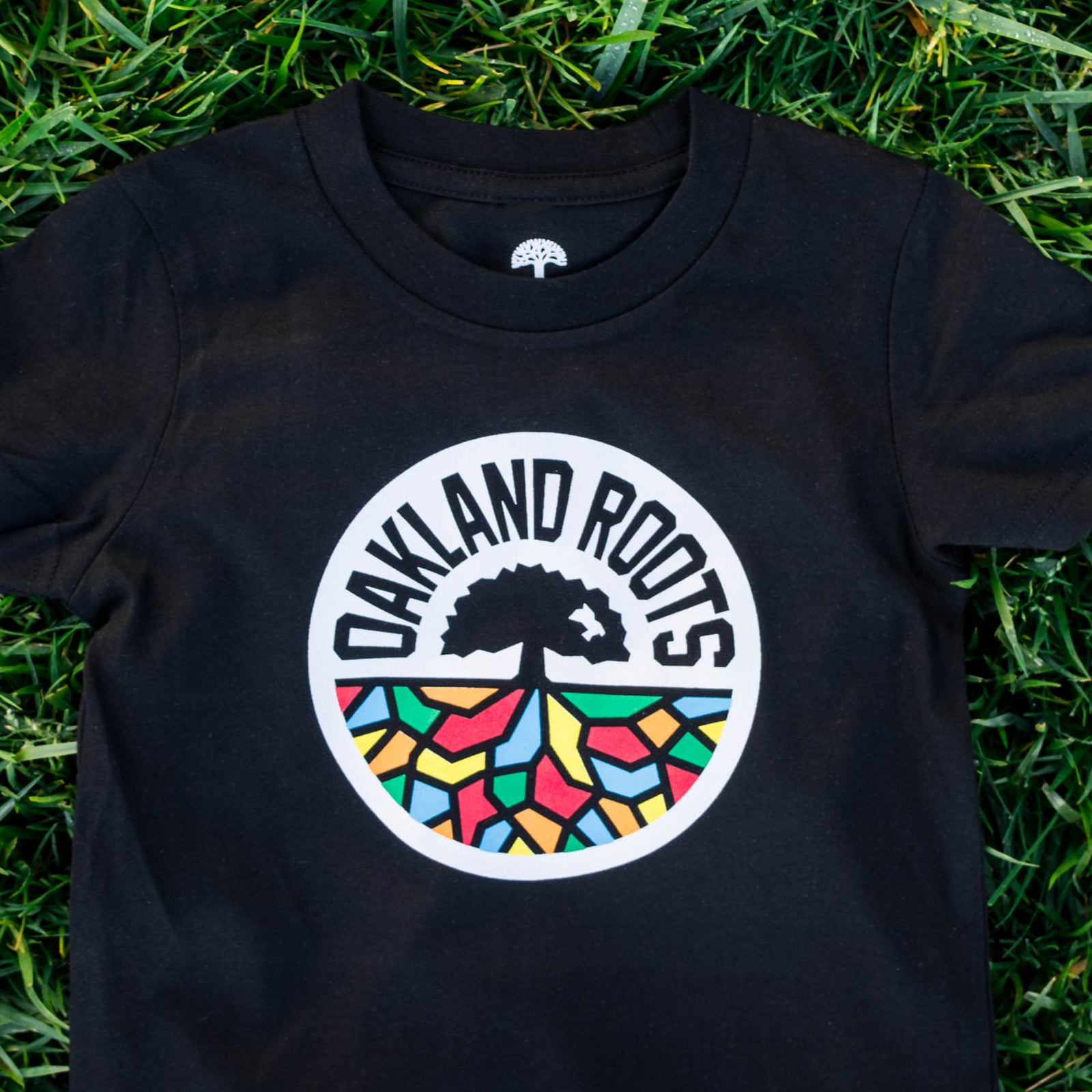 Three-quarter view of a black toddler sized t-shirt with a full-color Roots SC logo on the chest