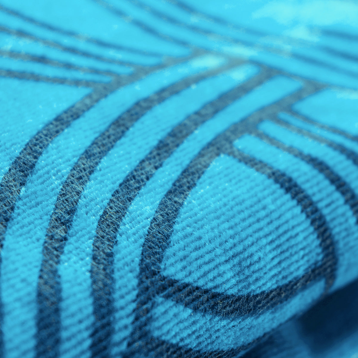 Close-up view of the Oaklandish Classic Logo Beach Towel, an oversized plush beach towel made from cotton terry velour, featuring a detailed pattern of dark blue lines and curves. The fabric's texture is visible, with small fibers and a slightly ribbed surface, creating an abstract, geometric design accentuated by the contrasting colors.