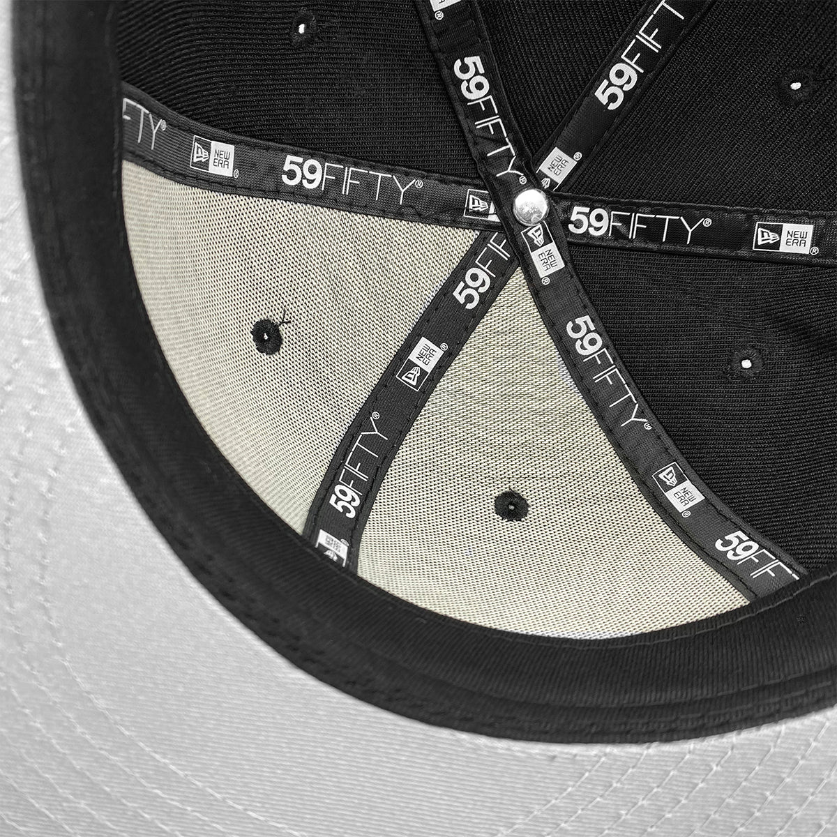 The image showcases the interior of a black and grey New Era X Oaklandish Classic 59FIFTY Fitted Cap. The inside labels feature the "59FIFTY" text alongside the New Era and Oaklandish logos, sewn into the inner seams of the fitted structured crown. A light grey sweatband is visible around the bottom, with light filtering through to create a semi-transparent effect.