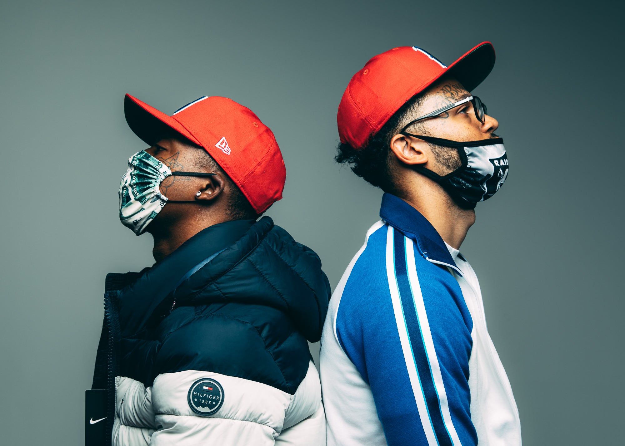 Khalil & Tre, with their backs to each other both wearing masks and red hats.