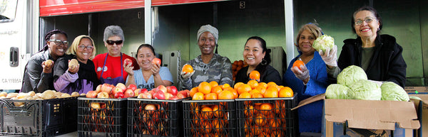 Various people posing with fruits and vegetables in crates and boxes.