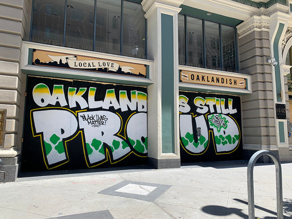 Oaklandish storefront boarded up but mural Oakland is still proud is painted on the boards.