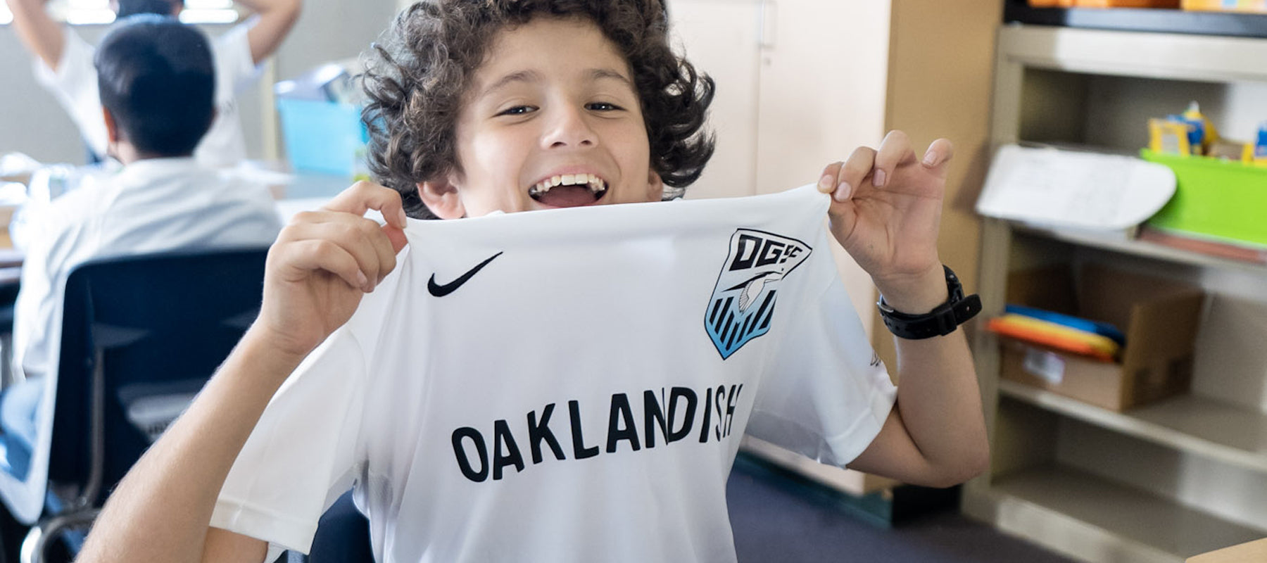 Kid smiling in classroom wearing Oakland Genesis Soccer Jersey