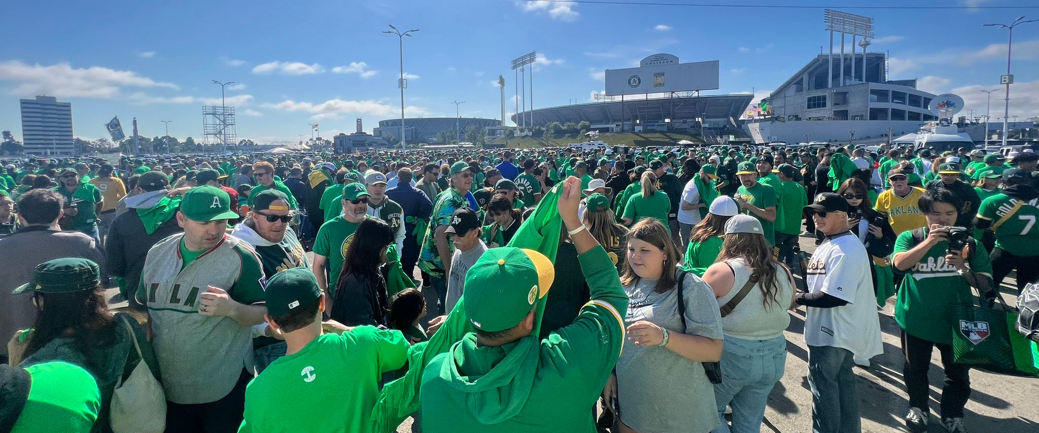 Photo of a crowd in the parking lot outside the baseball stadium in Oakland, CA on reverse boycott day, tailgating and handing out kelly green SELL tees