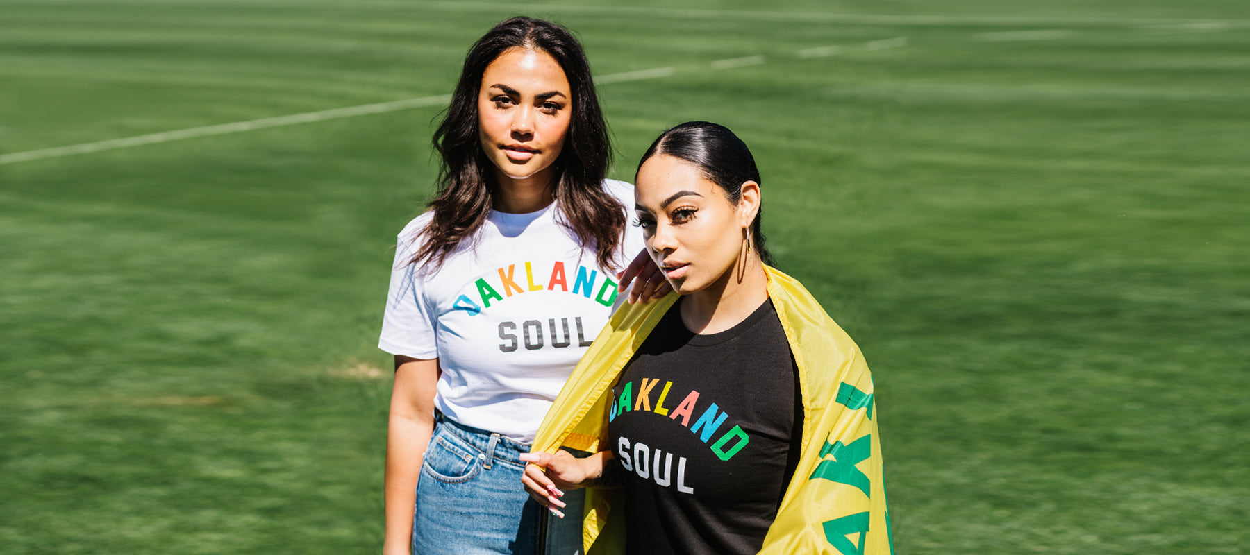 Two women standing on soccer field both wearing Oakland Soul Wordmark T-Shirts.