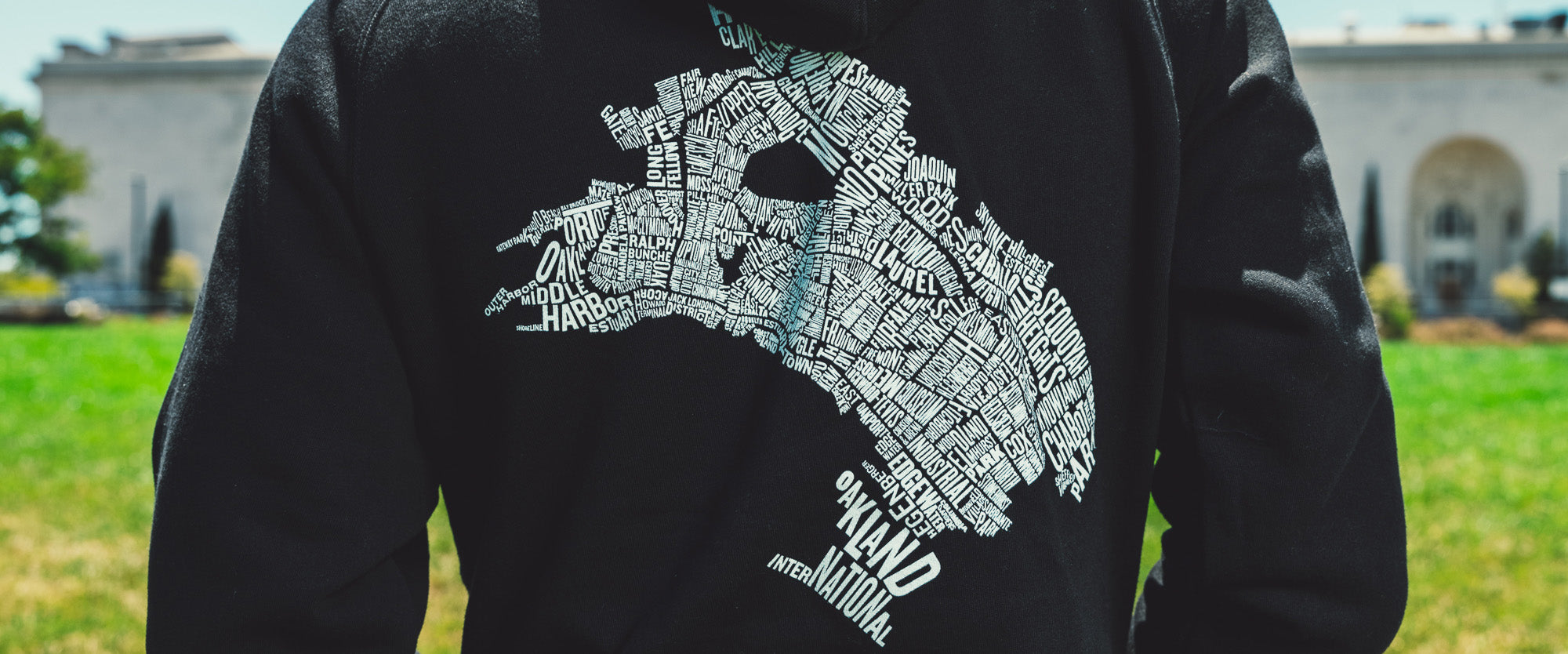 A man on the with a view of the backside of his black zip hoodie with a graphic of an Oakland neighborhood map.
