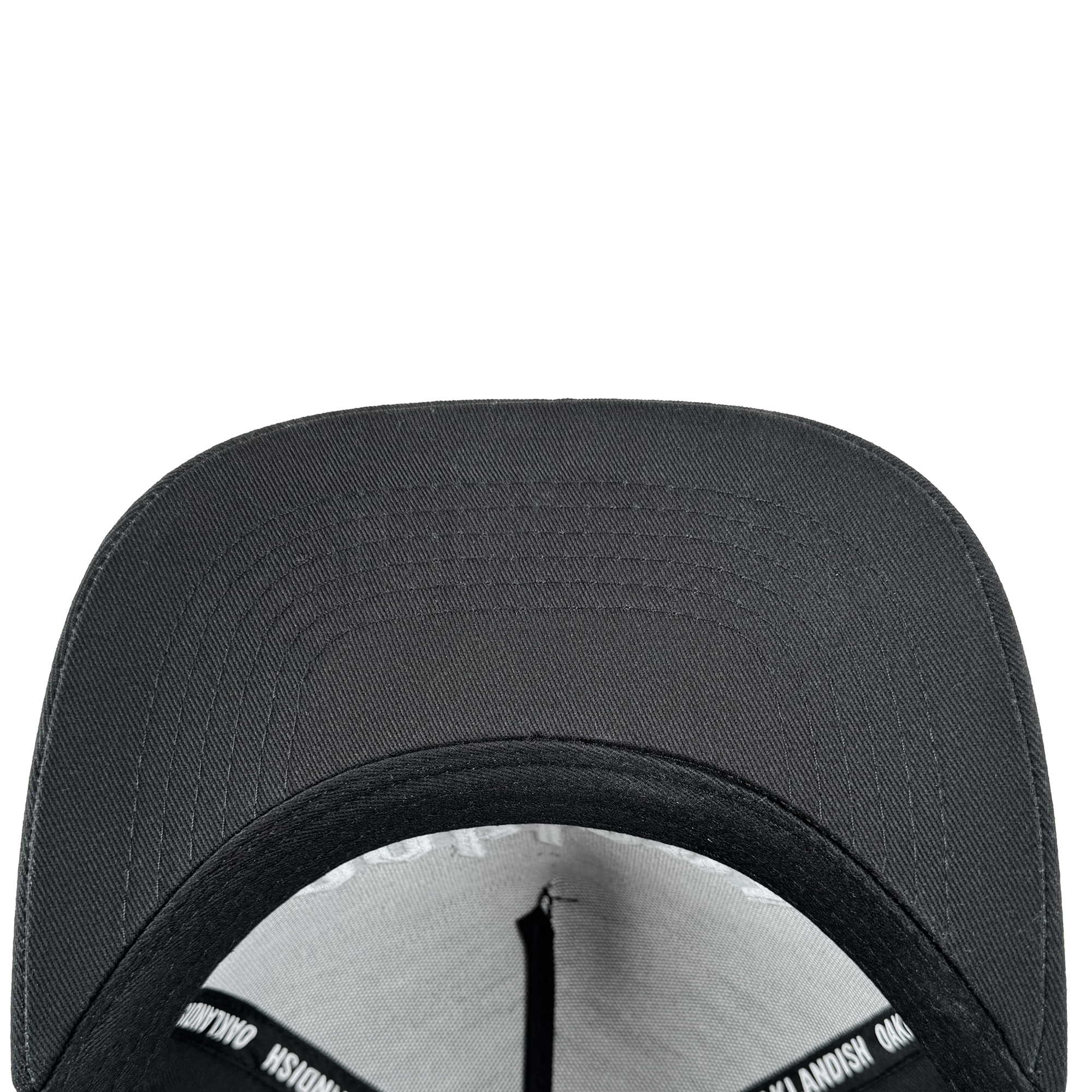A close-up, top-down view of the Oaklandish Oakland 68s Panel Cap highlights its curved brim, textured fabric, interior sweatband, and a black lining with white text, all set against a plain light gray background.
