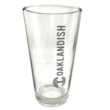 Close-up of clear 16 oz glass beer pint glass with dark grey Oaklandish logo and wordmark imprint.