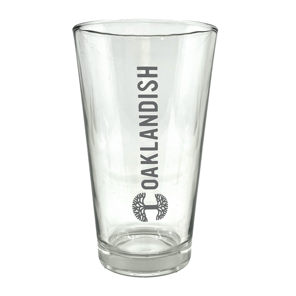 Clear 16 oz glass beer pint glass with dark grey Oaklandish logo and wordmark imprint.