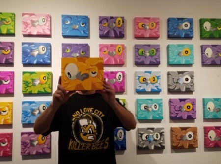 Artist, Nite Owl holding art in front of art display.