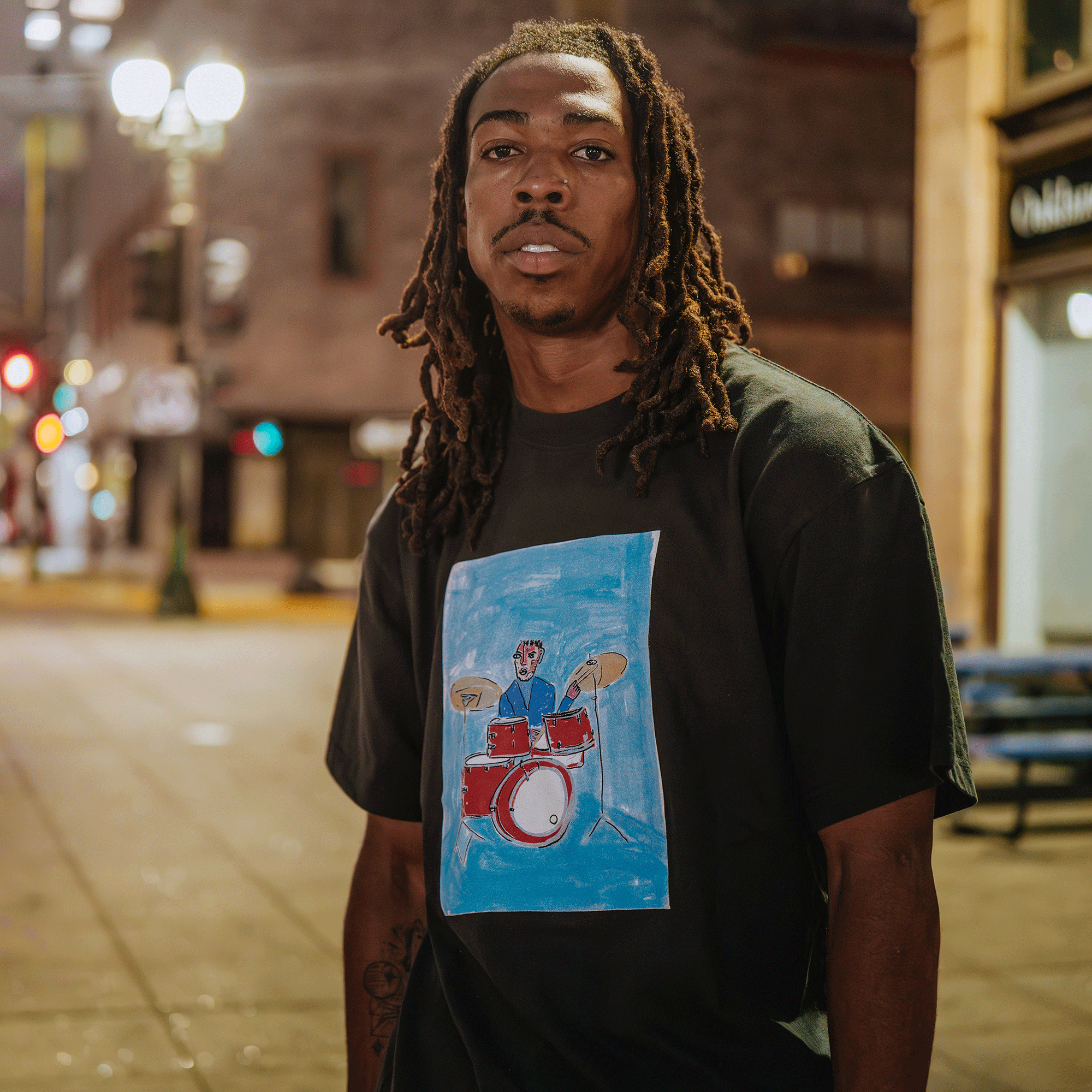 Man wearing a black t-shirt with a colorful graphic design on a city street at night.