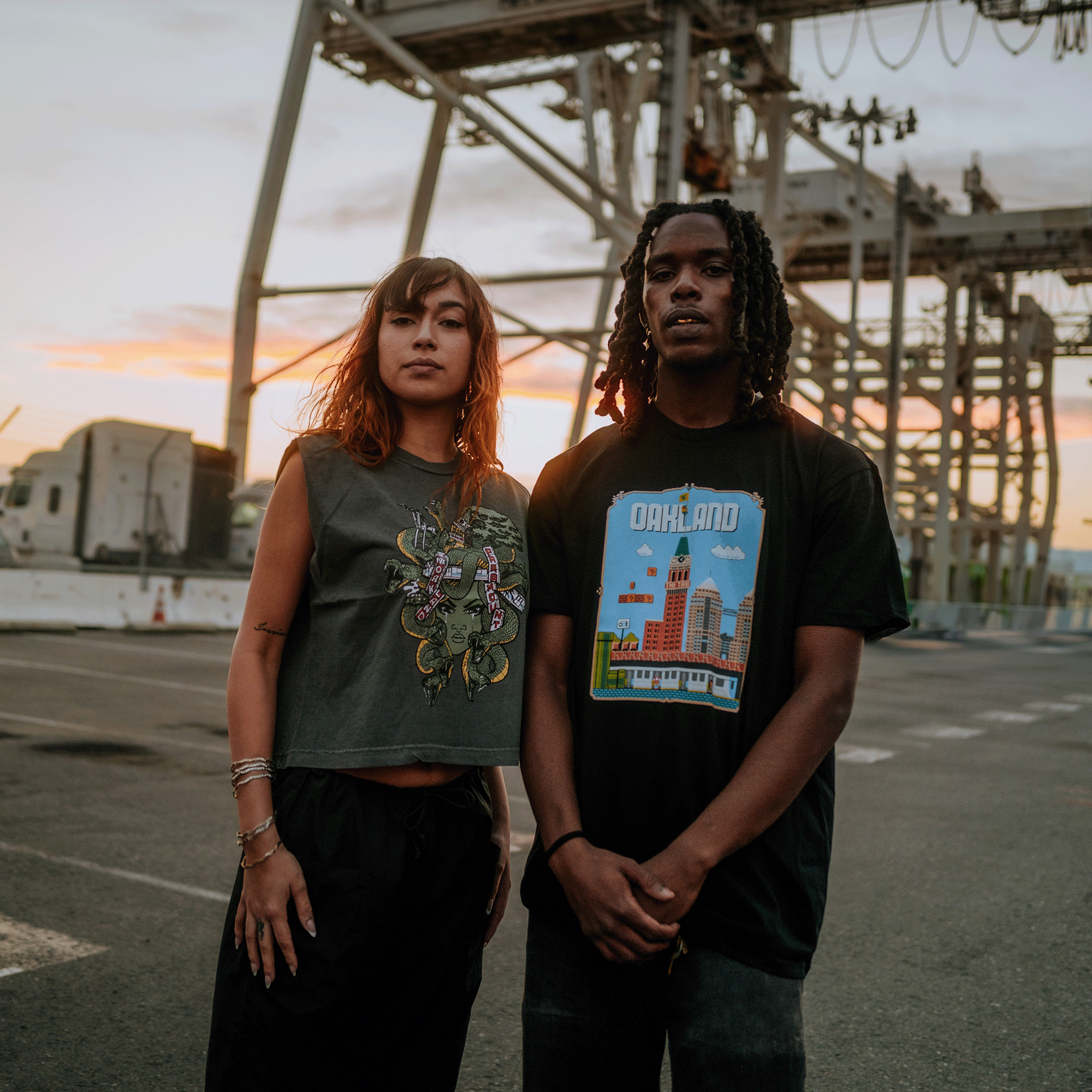 Female model standing with male model wearing black t-shirt with Super Mario style graphic with Oakland cityscape.