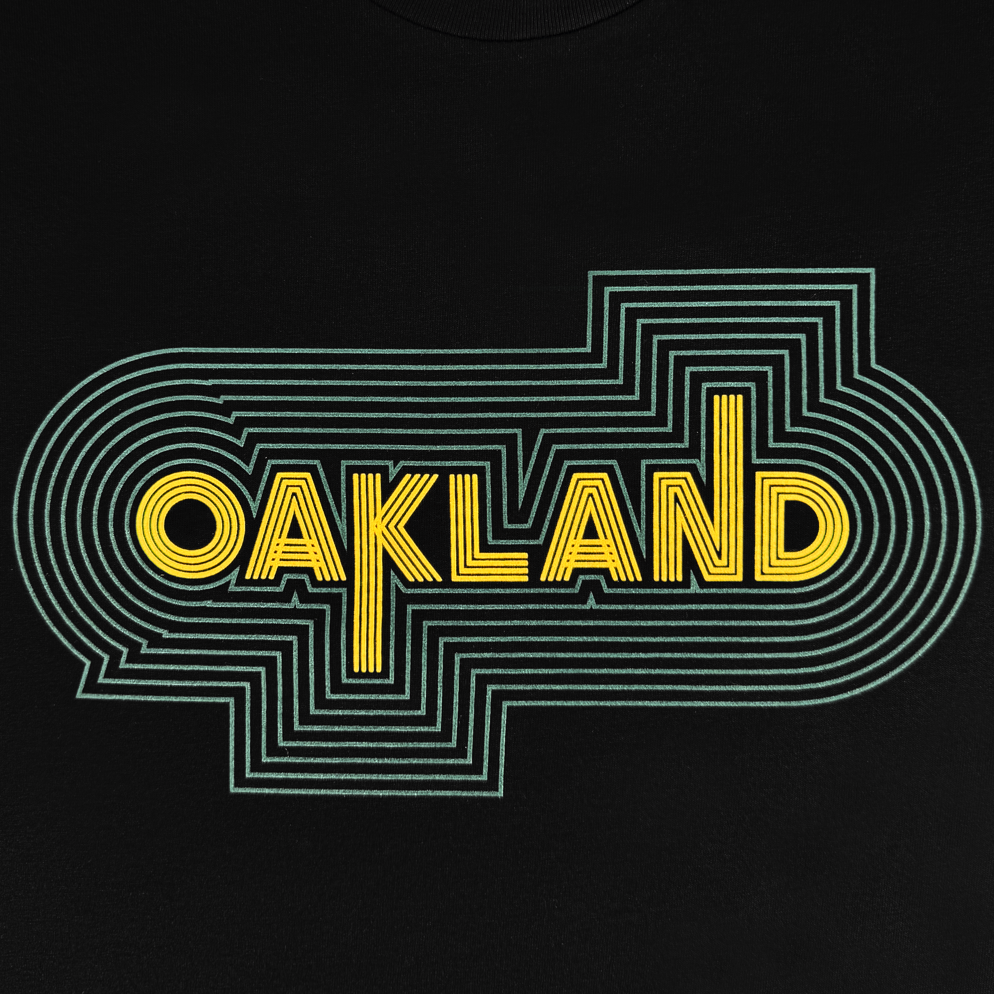 The "Oakland Sports Culture '68 Tee" by Oaklandish showcases "OAKLAND" in bold yellow block letters with a green, geometric outline on black, capturing a retro sports vibe and maze-like design reminiscent of the energetic spirit of iconic events like the Olympics '68.
