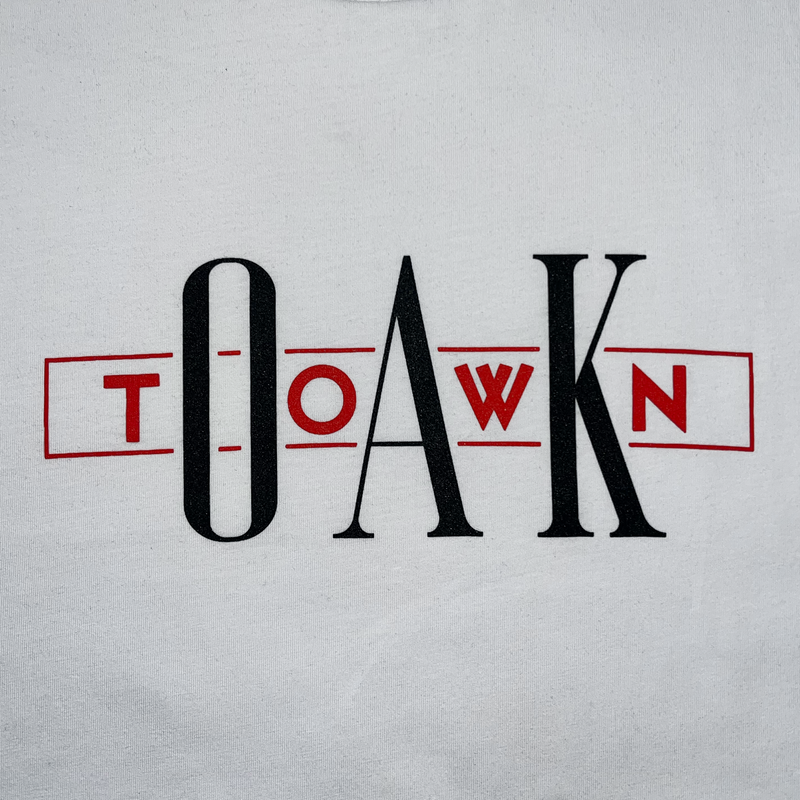 Close up image of white t-shirt with OakTown printed at center in red and white ink.