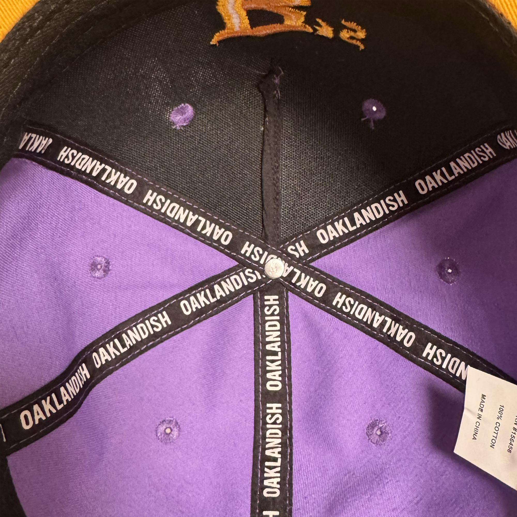 The inside of an Oakland Ballers 5 Panel Cap, featuring branded black taping with white text, a white tag, and purple stitching along the fabric panels. The top button is silver, and the inner brim displays black and gold detailing—an eye-catching accessory from Oakland Ballers inspired by local baseball team pride.