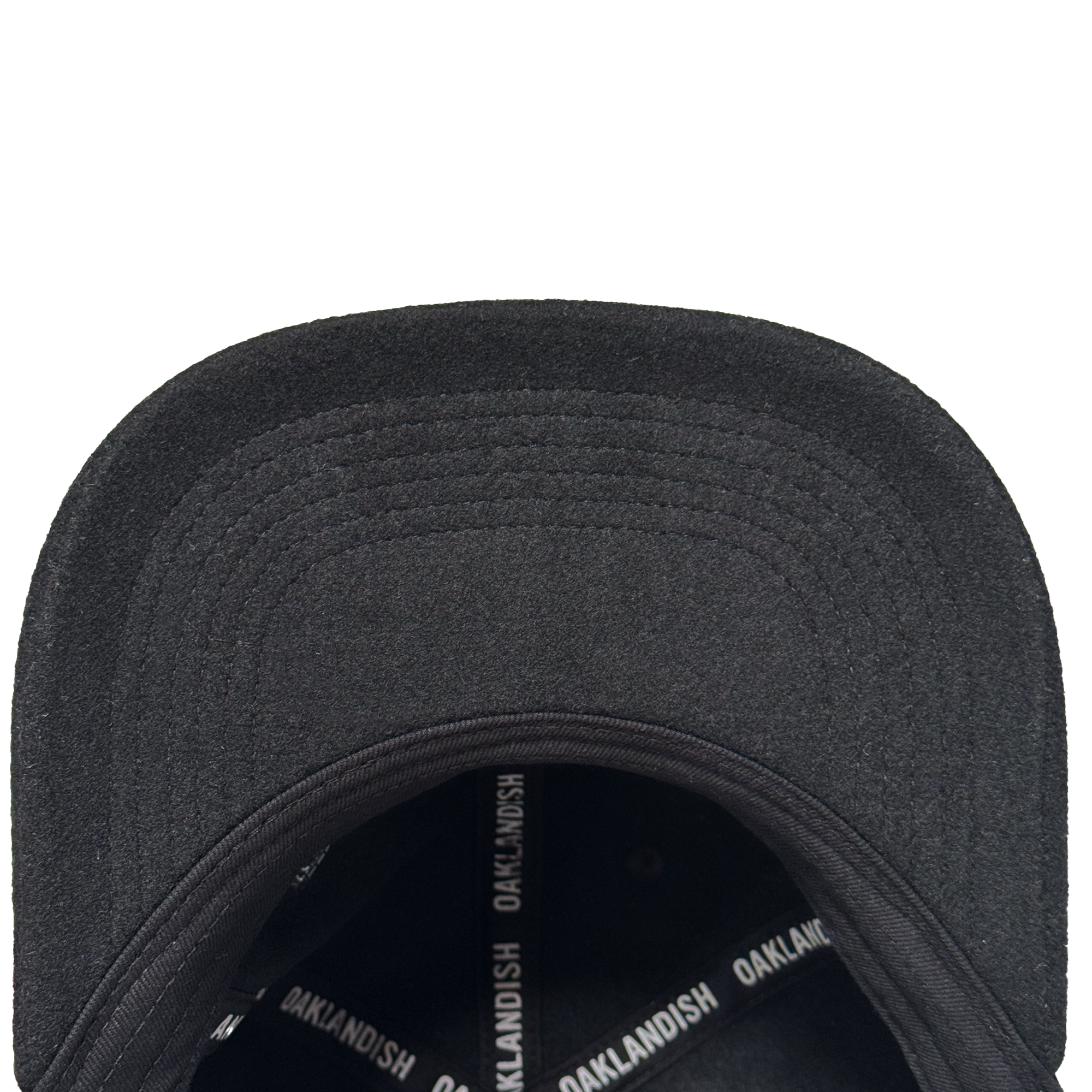 A top-down view of the Oakland Ballers Felt Applique Strapback, a black polyester-wool blend hat from Oakland Ballers. Its curved brim and internal black bands with repeated white “OAKLANDISH” text stand out on a white background.