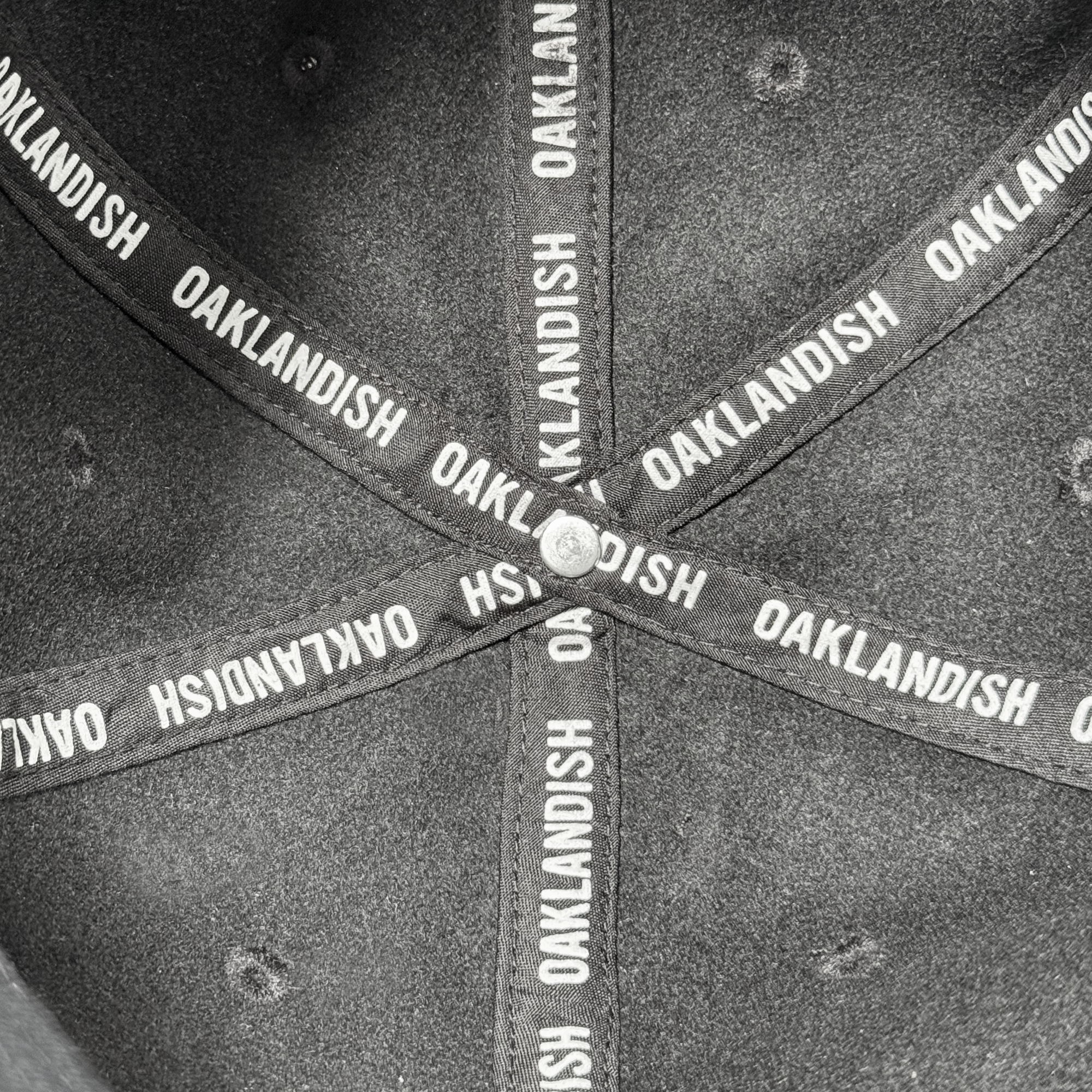 Close-up of the inside of the Oakland Ballers Felt Applique Strapback hat, featuring intersecting black bands with repeating "OAKLANDISH" print, a silver center button, and durable polyester wool blend by Oakland Ballers.