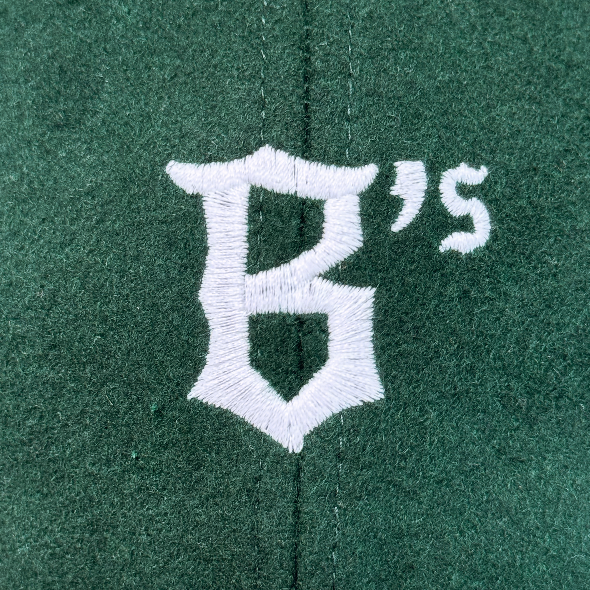 White embroidered text on green fabric features a bold "B" and sleek "s" in contrasting fonts, divided by a vertical seam—perfectly designed for the Oakland Ballers B Strapback by Oakland Ballers.