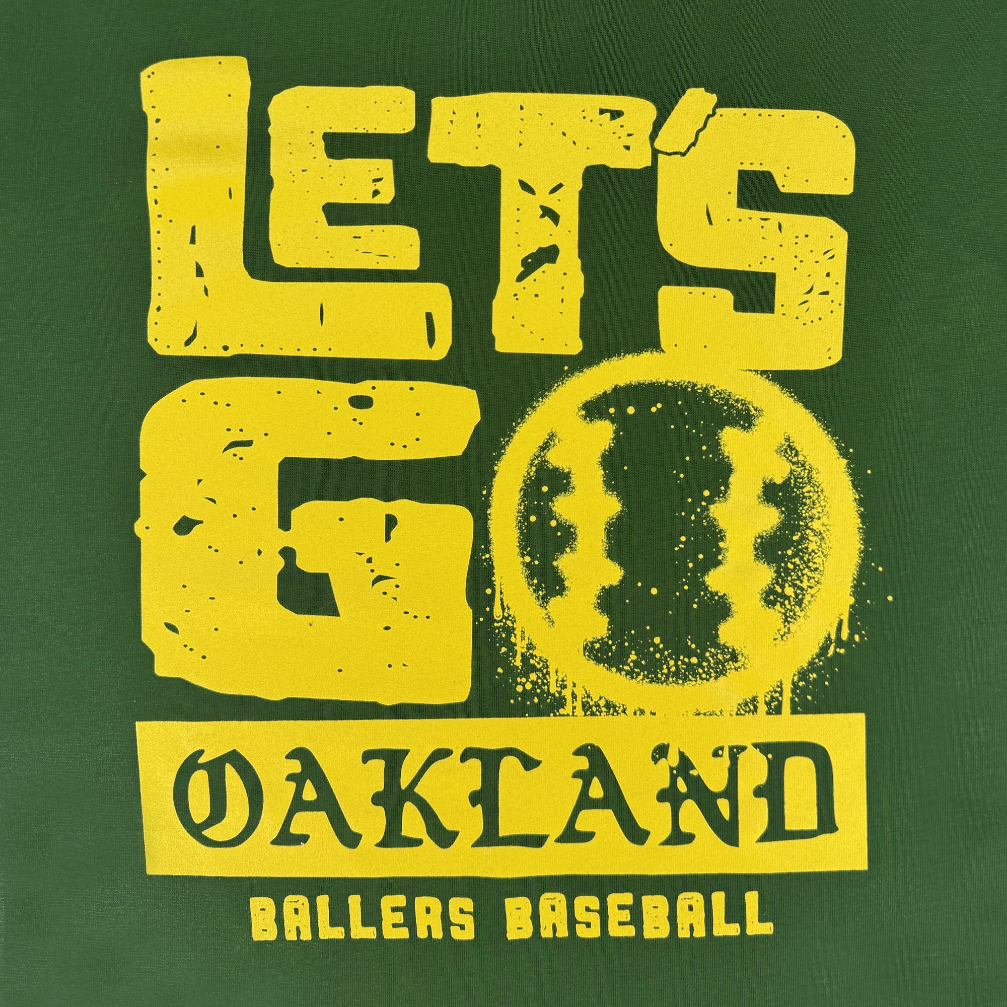 The Let's Go Oakland Tee by Oakland Ballers features a green background, bold distressed yellow "LET'S GO" over a baseball graphic, and "OAKLAND BALLERS" celebrating Oakland’s new pro Pioneer League baseball team. "BALLERS BASEBALL" in yellow at the bottom.