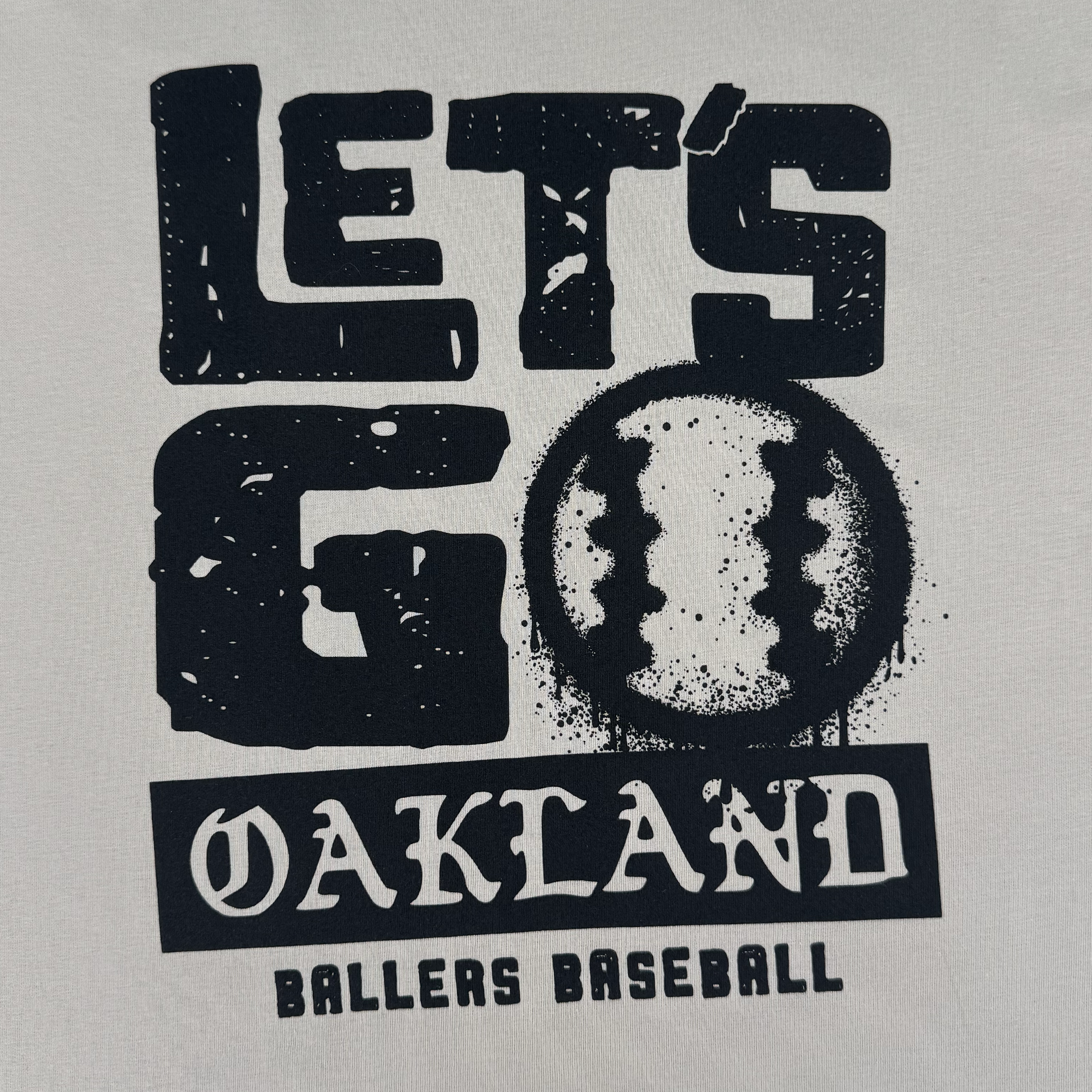 The Let's Go Oakland Tee by Oakland Ballers features black text on white, with “LET'S GO OAKLAND BALLERS BASEBALL” and a baseball-styled “O,” reflecting the team’s Pioneer League spirit and East Bay heritage.