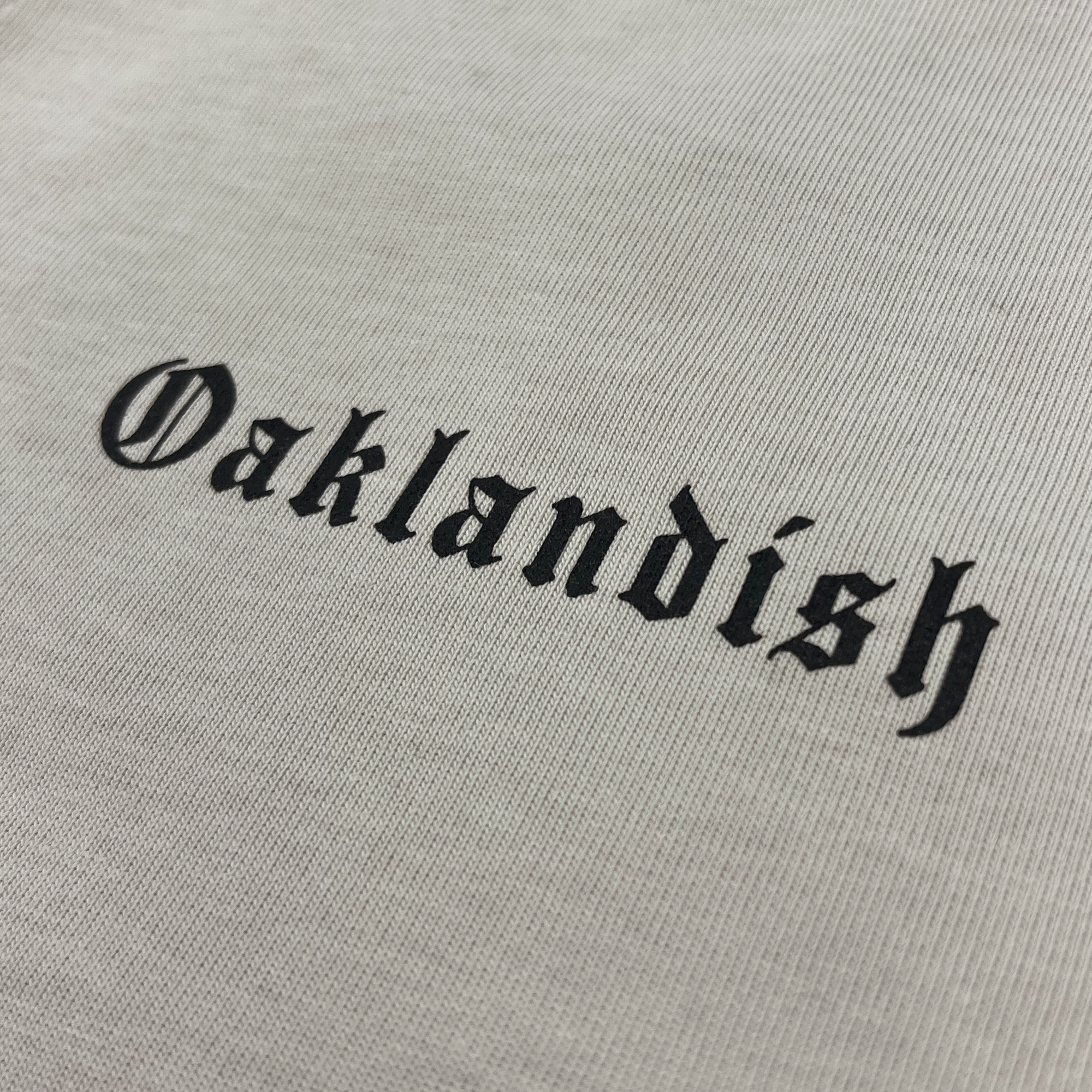 Detailed close-up of black OAKLANDISH wordmark in trip on a bone-colored baseball jersey.