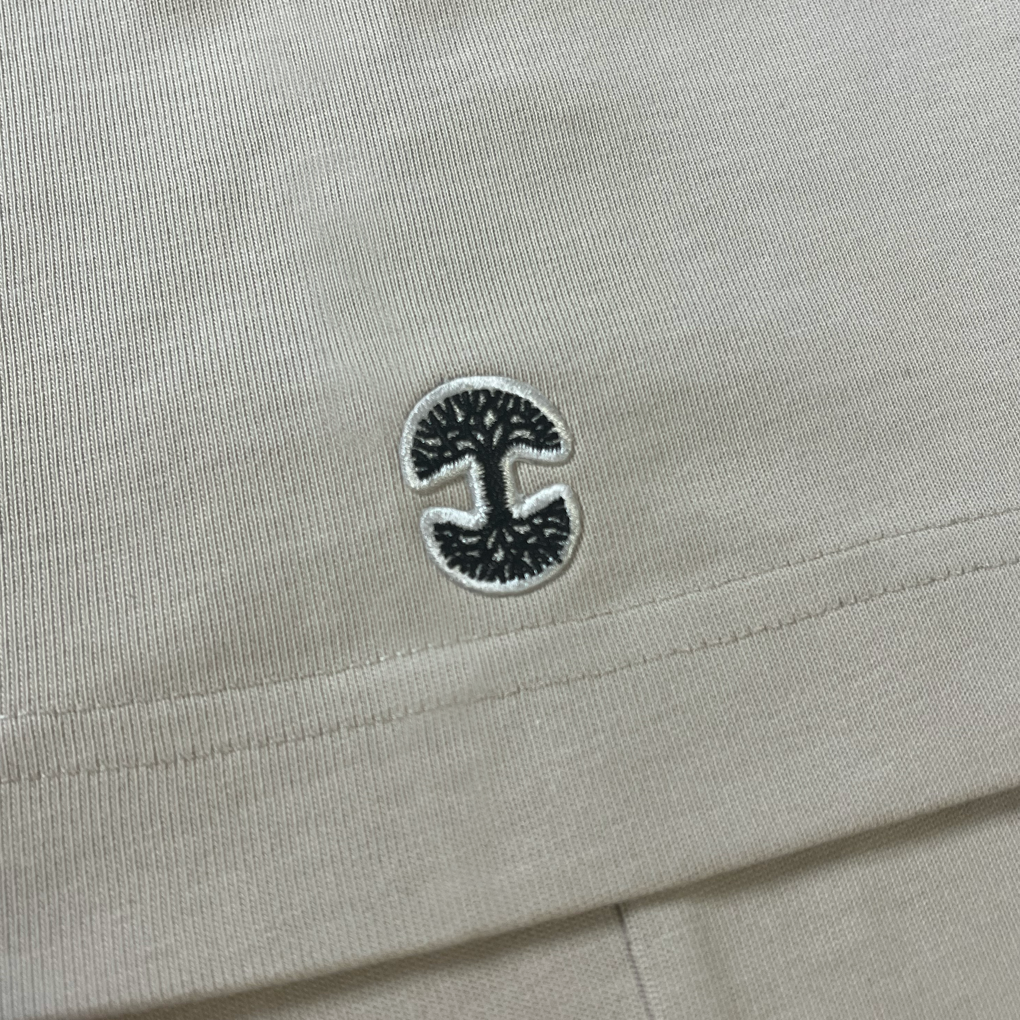 Detailed close up of Oaklandish tree logo patch on the sleeve of a bone-colored baseball jersey.