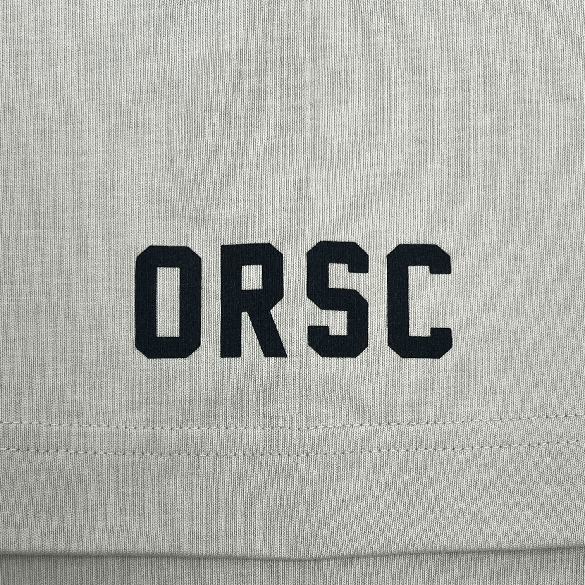 Detailed close-up of black ORSC wordmark on the sleeve of a bone-colored baseball jersey.
