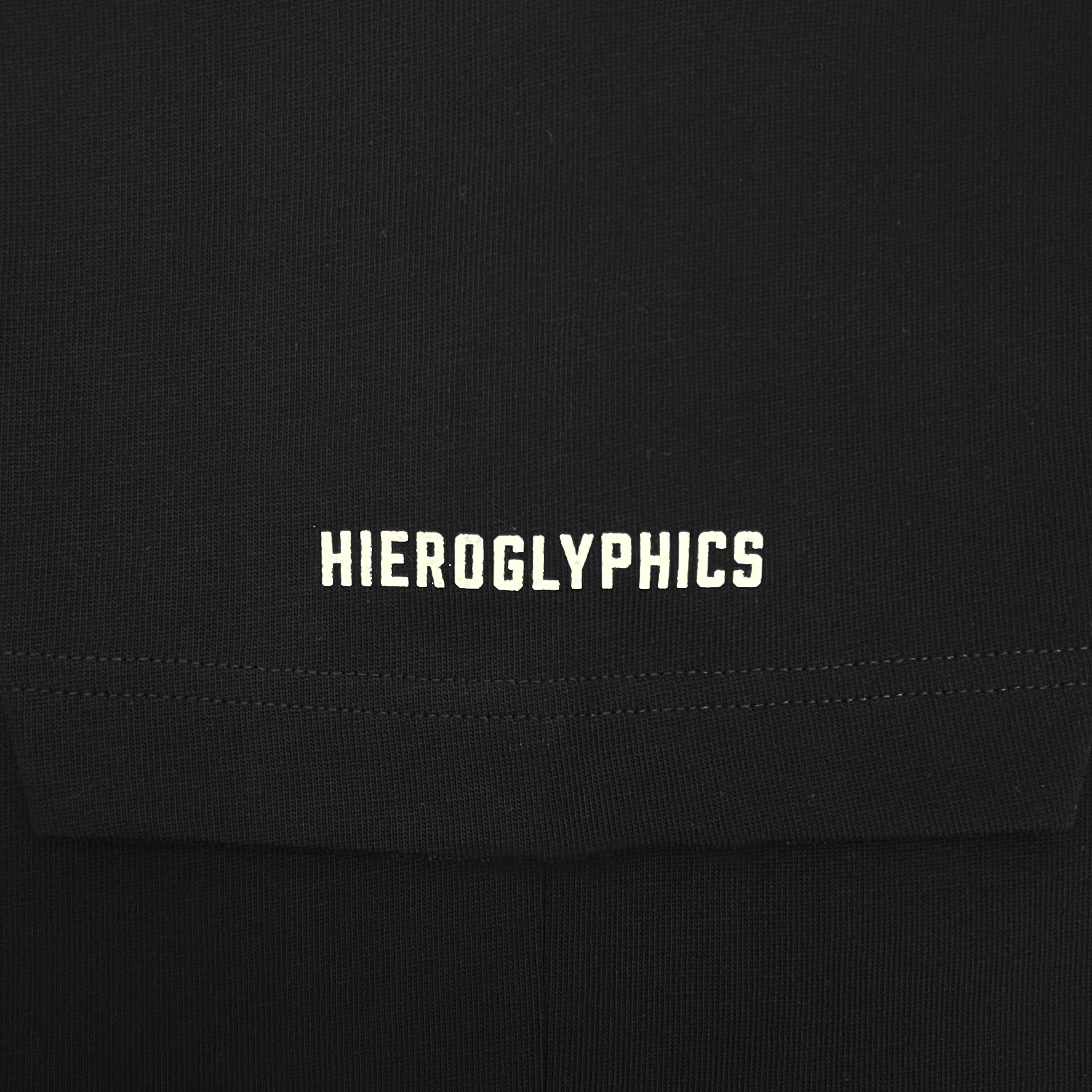 A close-up view of the Hiero Heavy Button-up Baseball Jersey fabric with the word "Hieroglyphics" embroidered in white text. The text is centered in the image, appearing clean and bold against the dark background of the material, which is available in men's sizing.