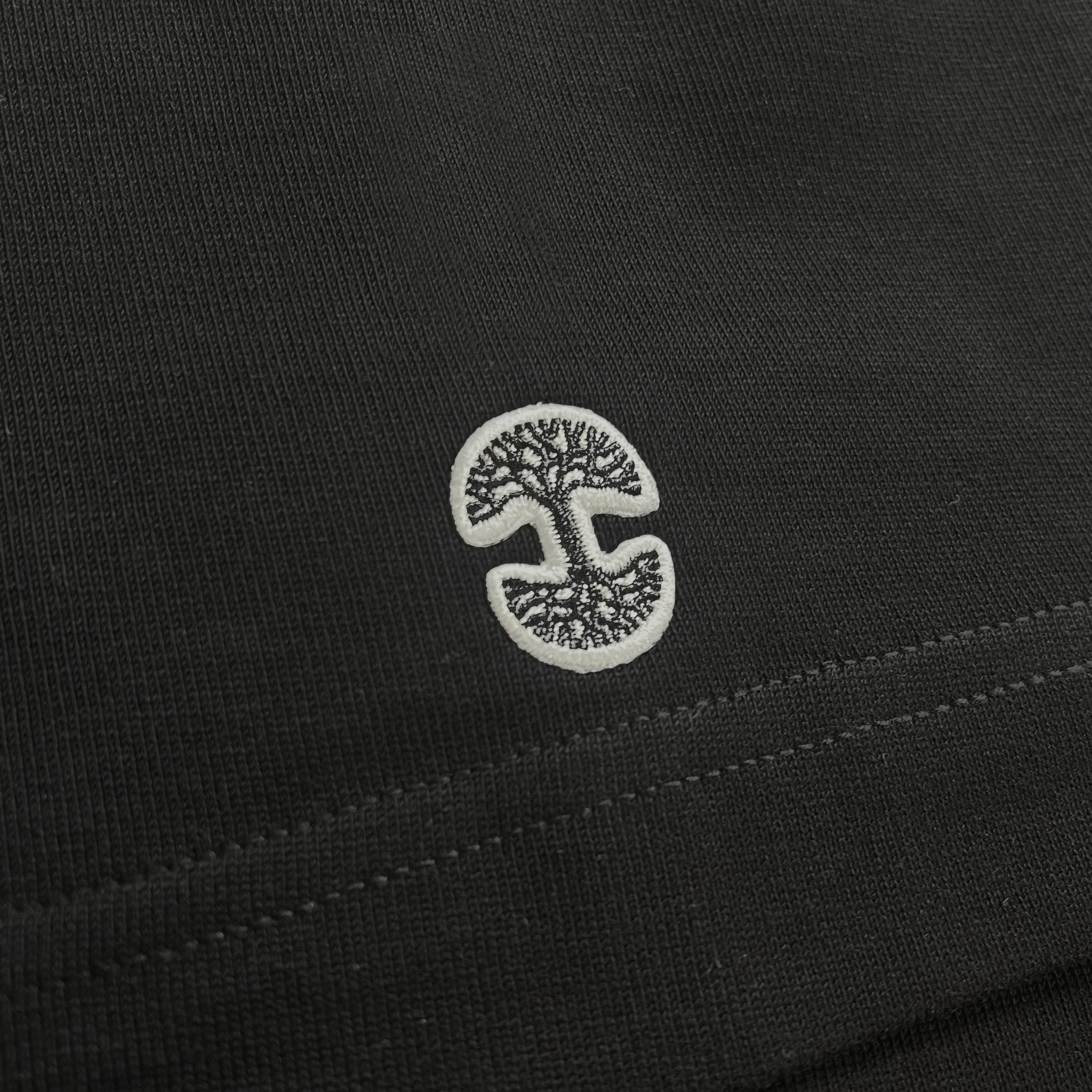Detailed close up of Oaklandish tree logo on the sleeve of a black baseball jersey.