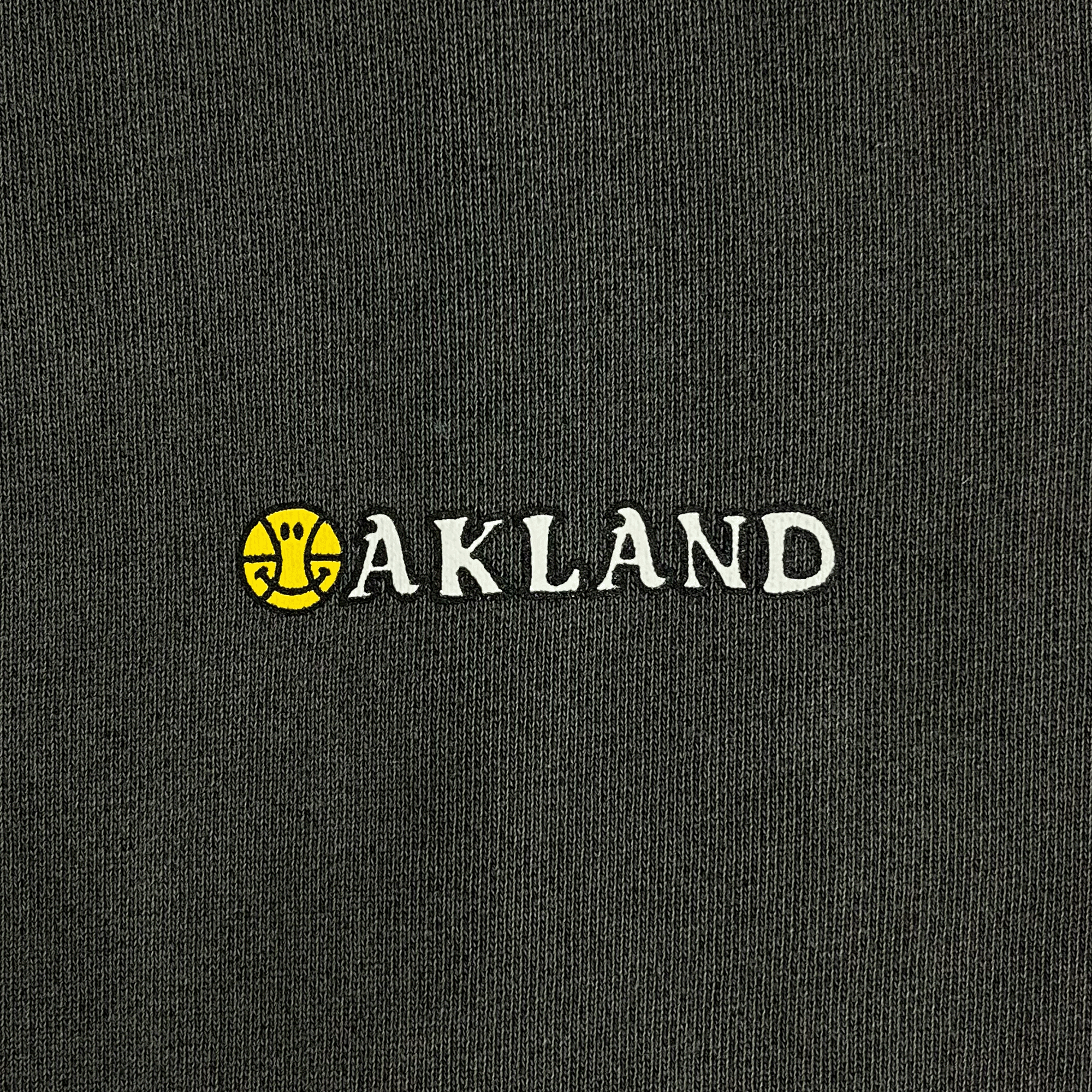 Close-up of OAKLAND wordmark with yellow basketball ball as the O on a pigment black pullover hoodie sweatshirt. 