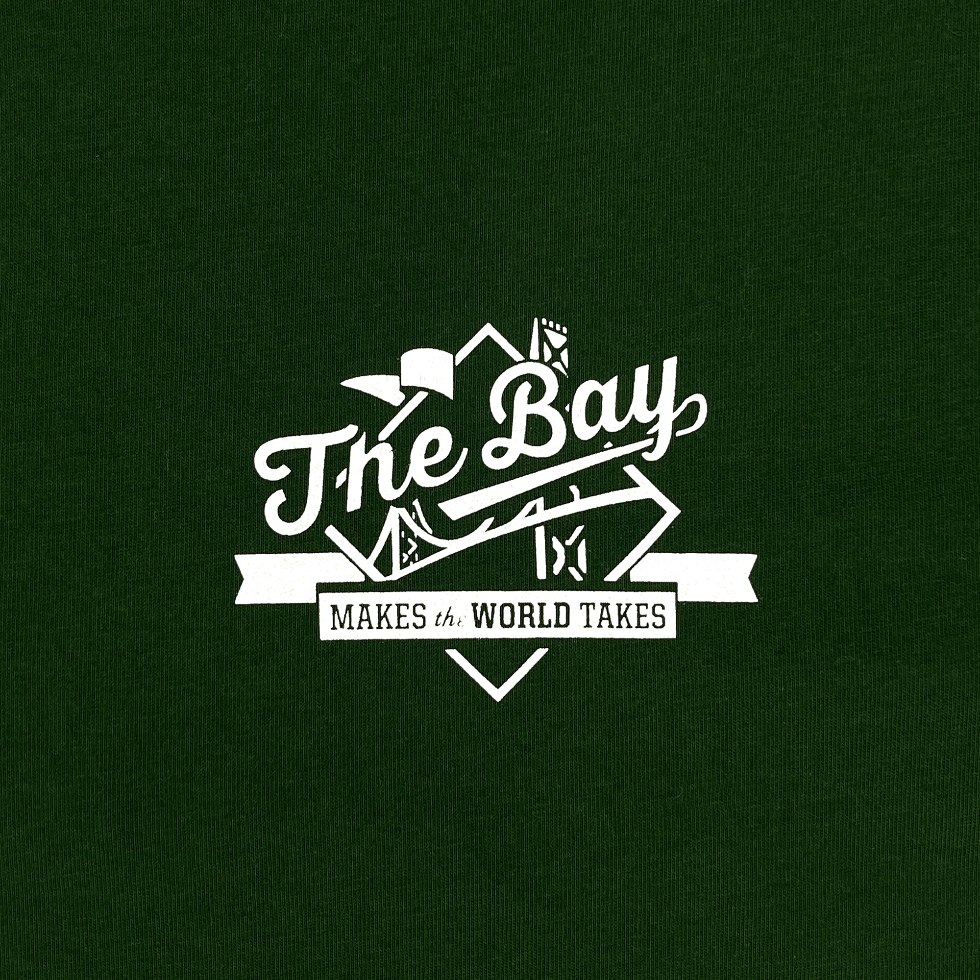 Close-up of a white The Bay Makes The World Takes logo graphic on the left chest wearside of a forest green t-shirt.