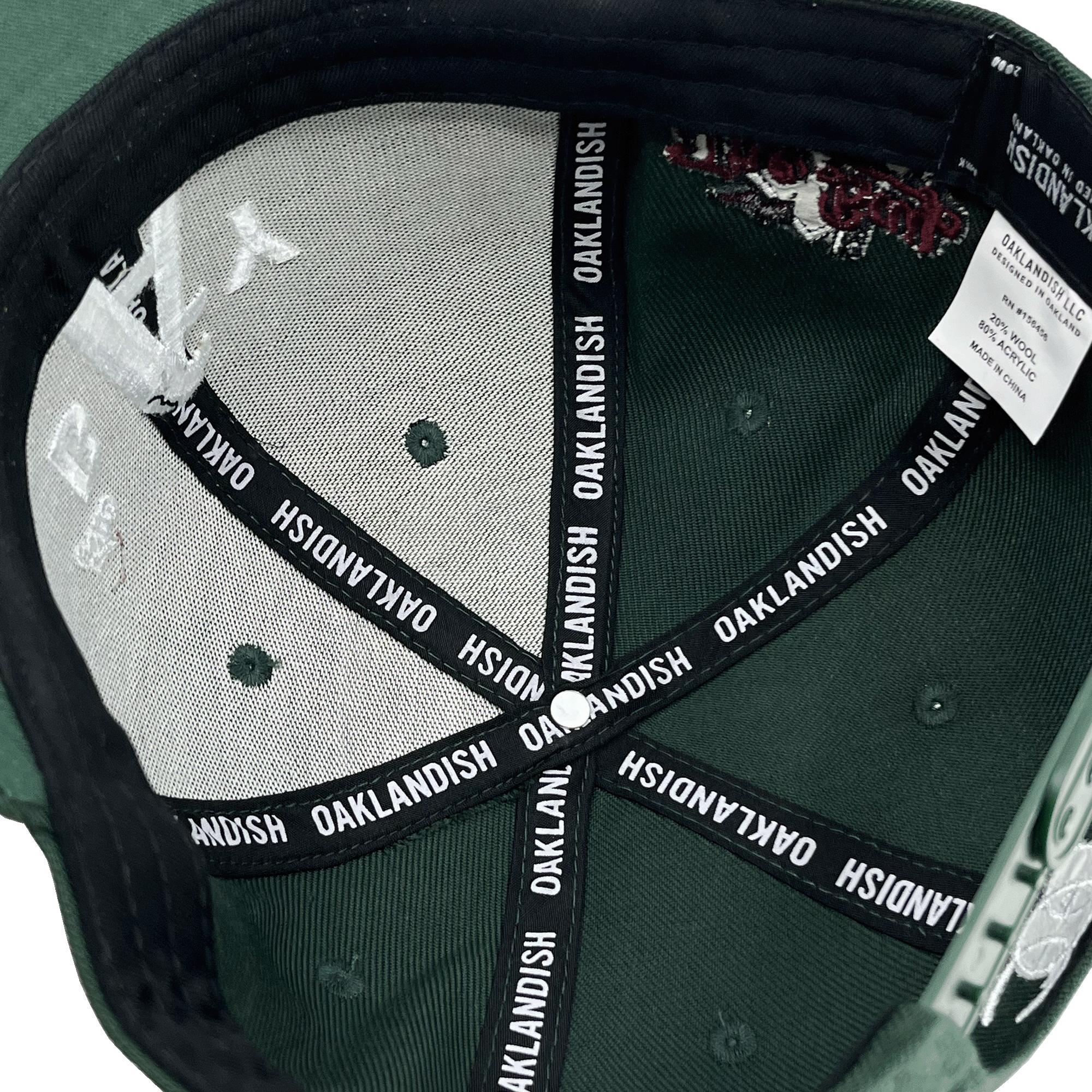 Inside crown view of a forest green hat with black striping with Oaklandish wordmark on repeat.