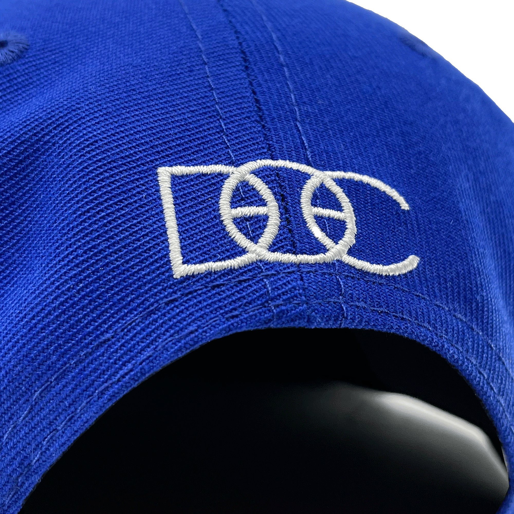 Close-up of white embroidered overlapping DOC wordmark on the back of a royal blue hat.