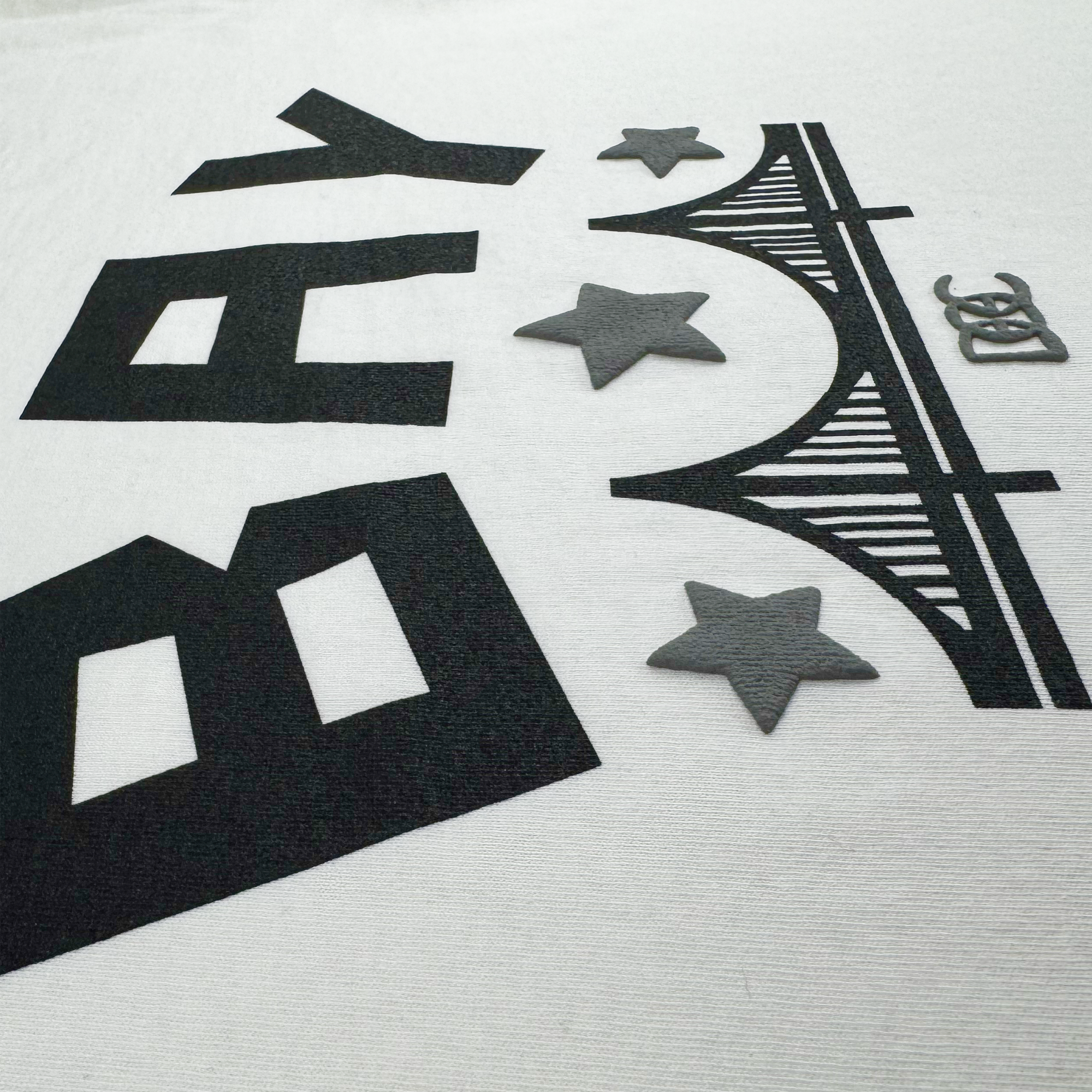 Black "BAY" letters on white, gray stars, a black bridge, and a metallic fist graphic—modern details from Oaklandish’s Bay Bridge Tee By DOC V2, perfect for a classic fit in heavyweight cotton.