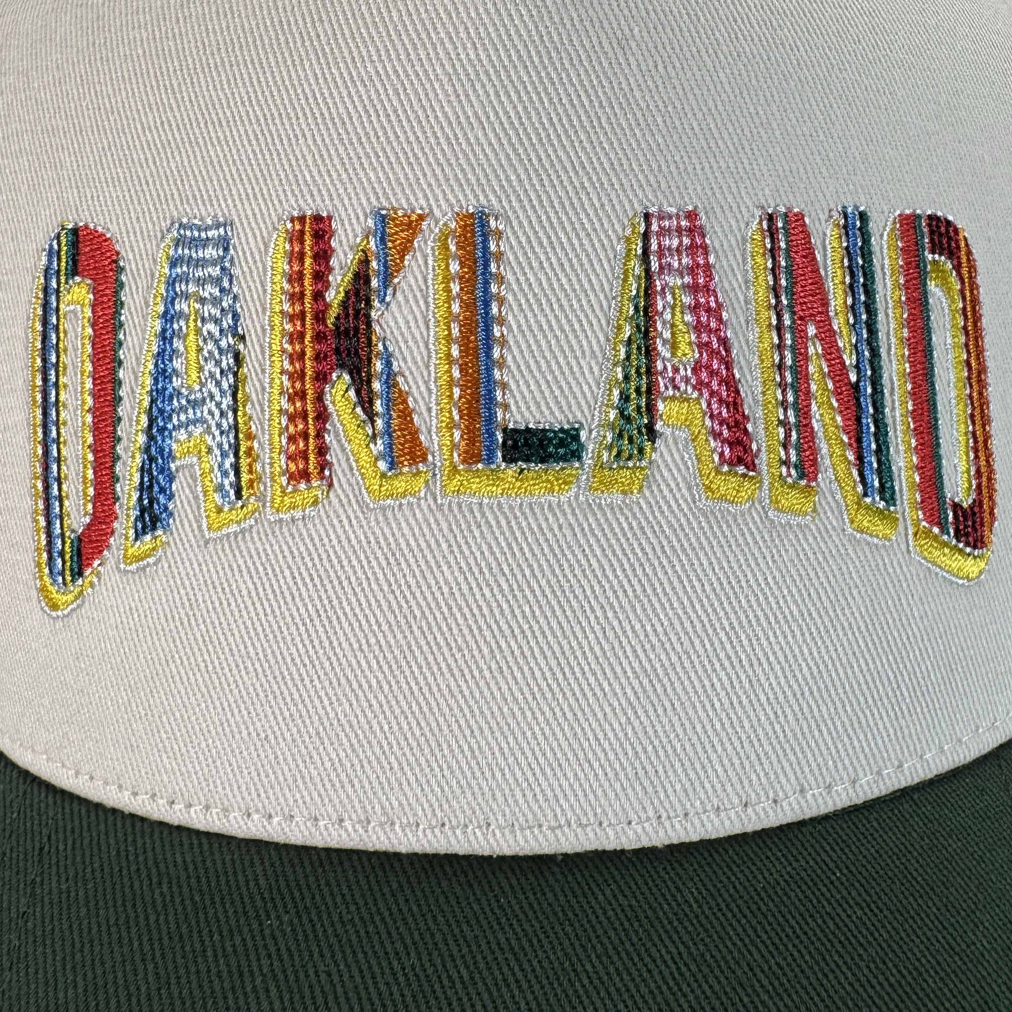 Close-up of the Oakland Beisbol 5 Panel Cap by Oakland Ballers, featuring "OAKLAND" in large, multicolored textured letters with yellow outlines and a dark green brim—an ideal accessory for any Oakland Ballers fan.