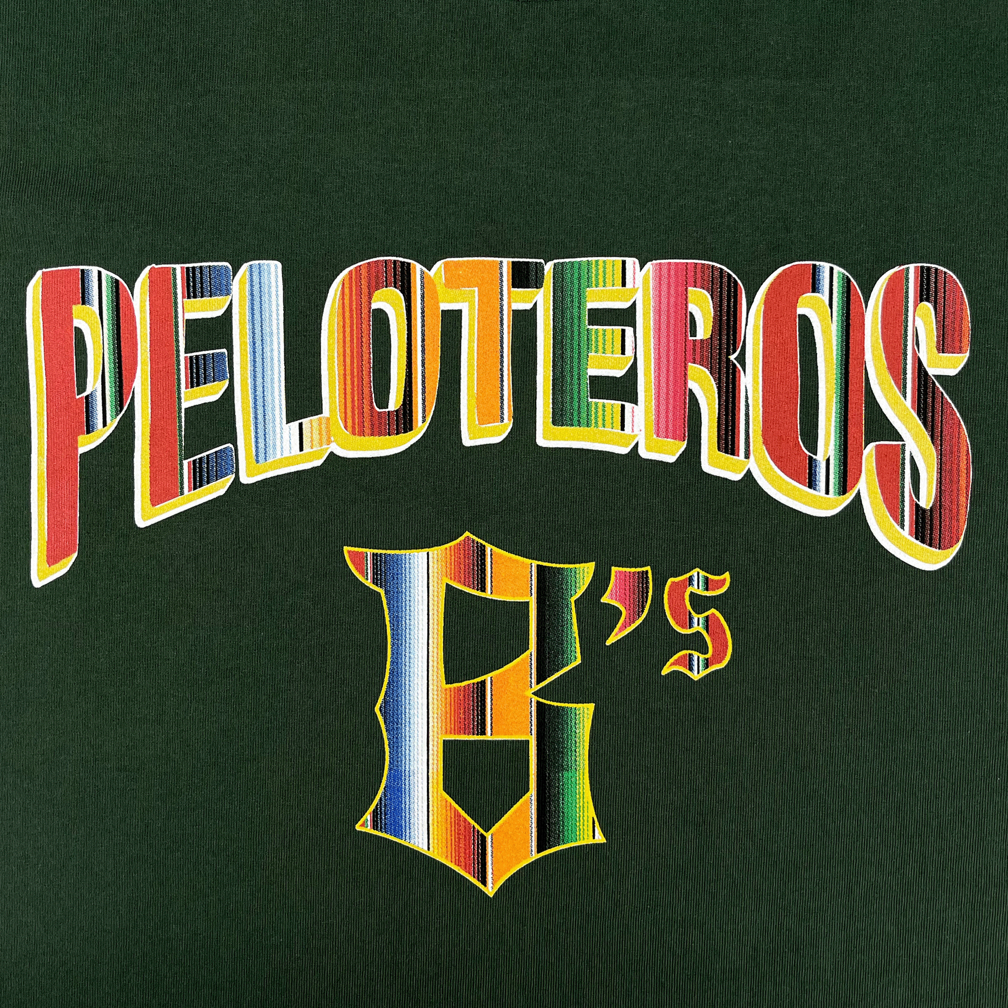 “PELOTEROS” appears in bold, multicolored letters above a matching stylized "E’s" on a dark green Oakland Beisbol Tee by the Oakland Ballers, with vibrant stripes inspired by traditional textiles.