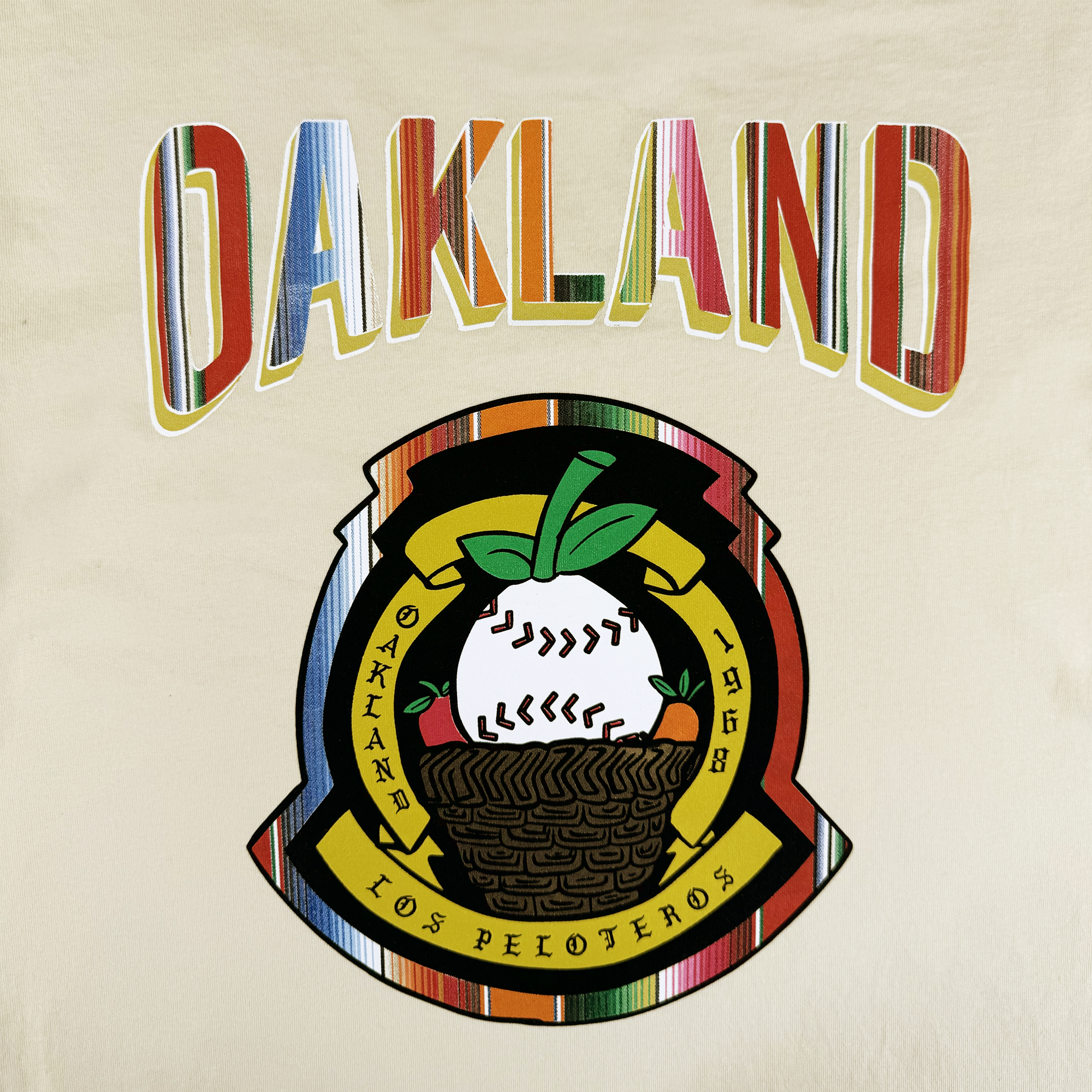 The Oakland Beisbol Tee by Oakland Ballers features “OAKLAND” in multicolored stripes above a lively baseball emblem, with a ring that reads “OAKLAND 1968 LOS PELOTEROS” in yellow for a bold, festive tribute to the team.