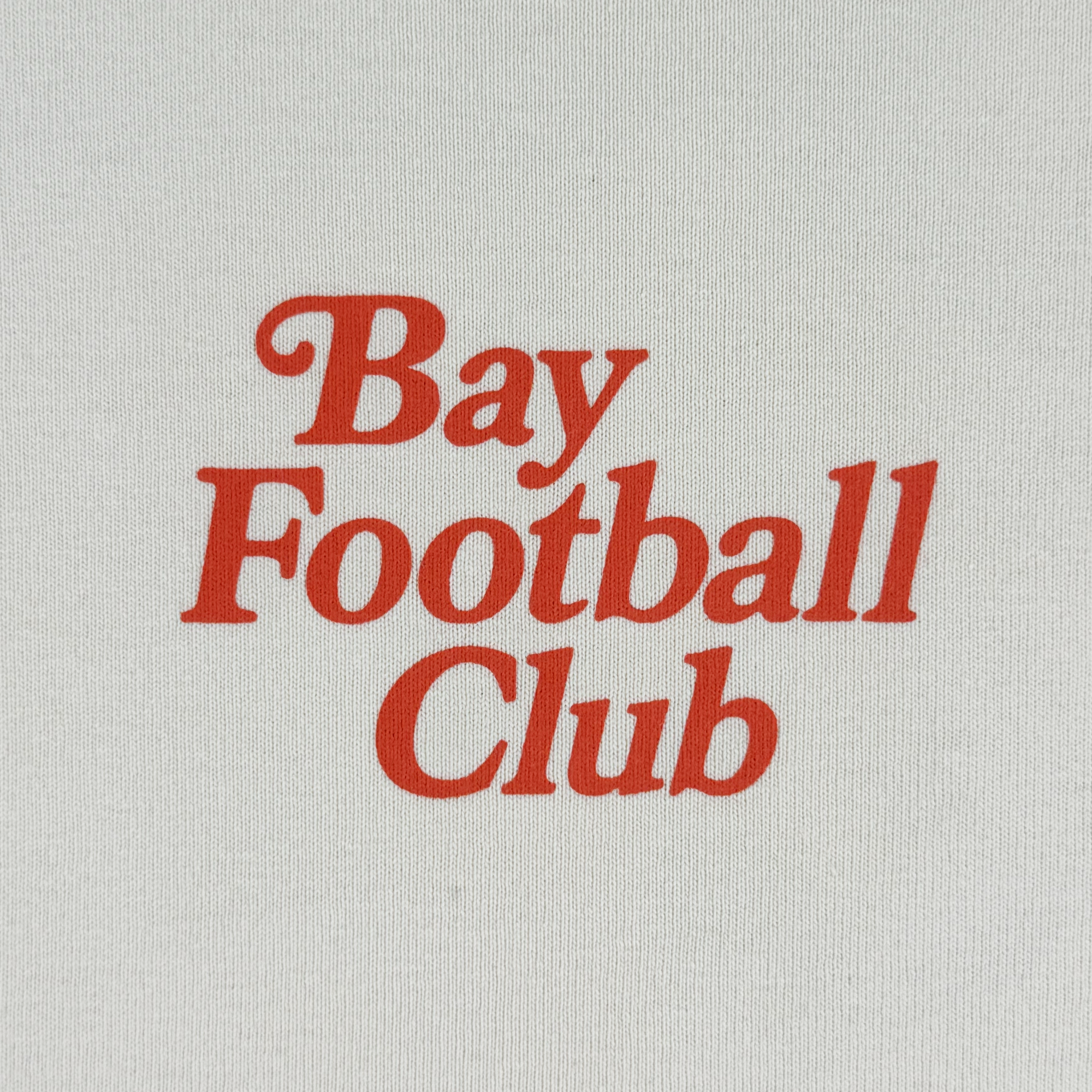 The Bay FC Jubilee Crew is a white sweatshirt with bold red "Bay Football Club" text stacked in a serif font, inspired by Bay FC. This clean, simple design is available in men's sizing.