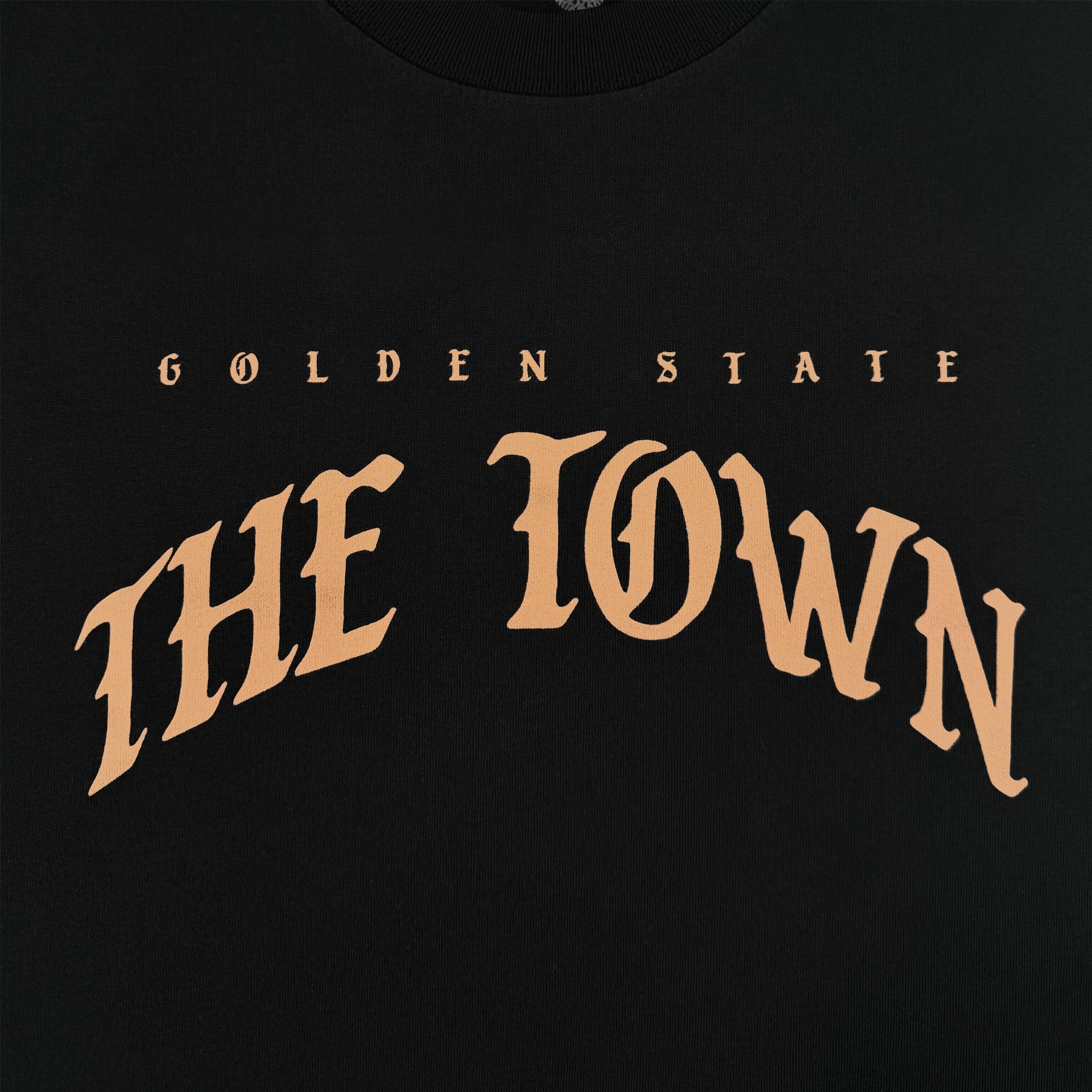 The GSW Arched Black-Letter Tee features bold tan "GOLDEN STATE" text above large, arched "THE TOWN" in stylized capitals on black—highlighted by an oversized “O” for signature Golden State Warriors style.