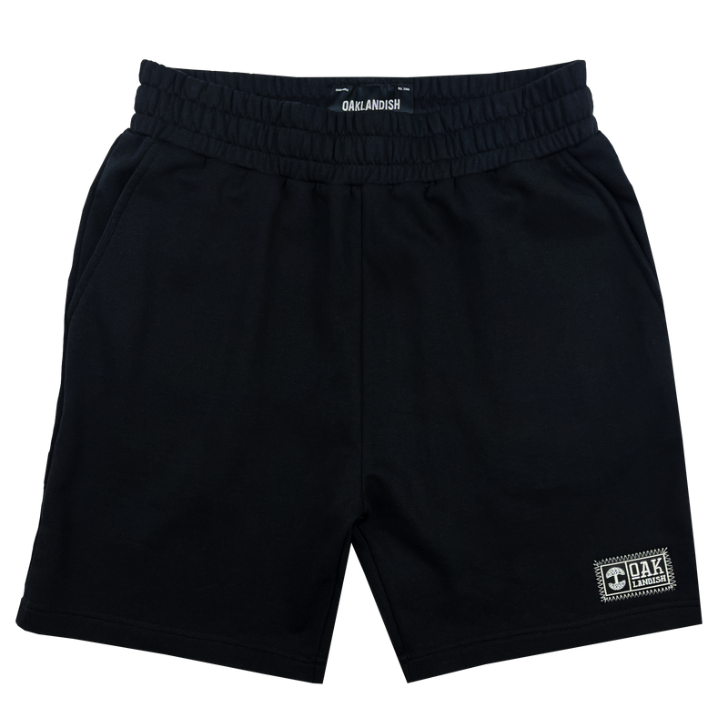 Front view of black fleece shorts with embroidered Oaklandish woven label near wearer's left leg hem.