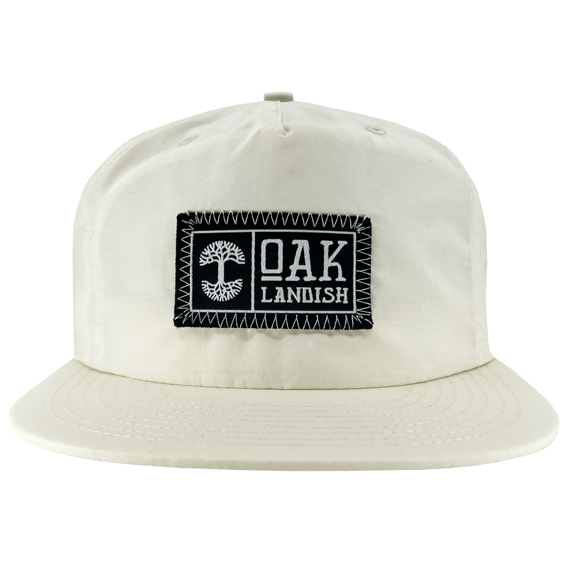 Front view of Ecru nylon snapback cap with embroidered Oaklandish black and white woven patch at center.