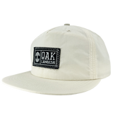 Side view of Ecru nylon snapback cap with embroidered Oaklandish black and white woven patch at center.