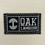 Close up image of heavy cotton ecru t-shirt with embroidered Oaklandish woven label on wearer's left chest.