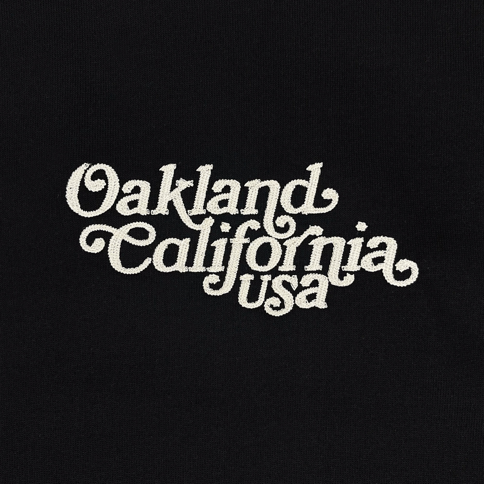 Close-up of white Oakland California USA script embroidered on the chest of a black t-shirt.