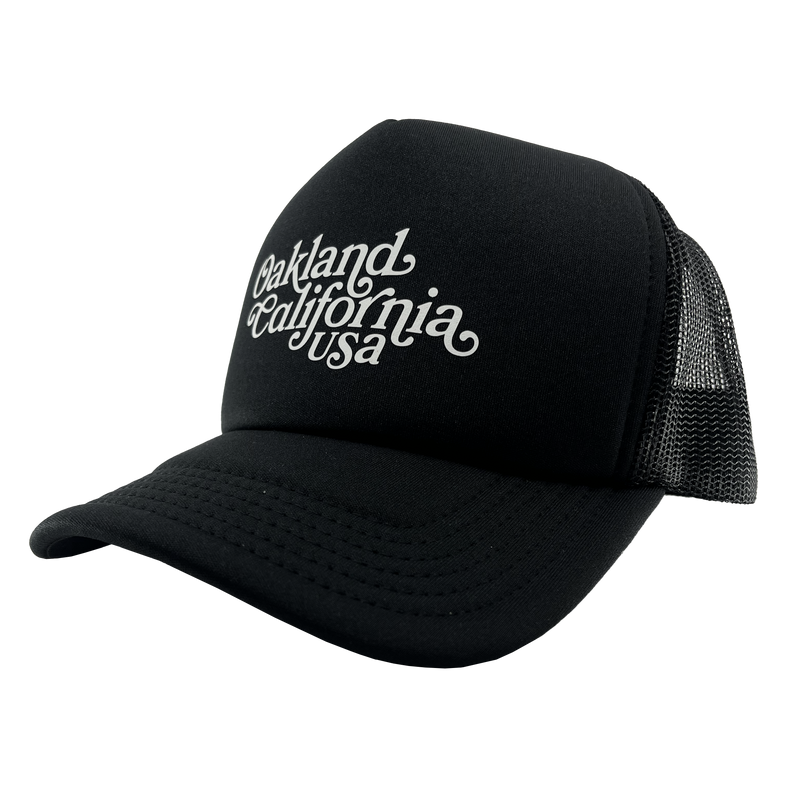Side view of a black trucker cap with foam front panel, mesh back, adjustable back, and white Oakland, California, USA wordmark on the crown.