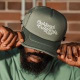 Male model wearing cypress bookman trucker hat with Oakland Califroania across the front.